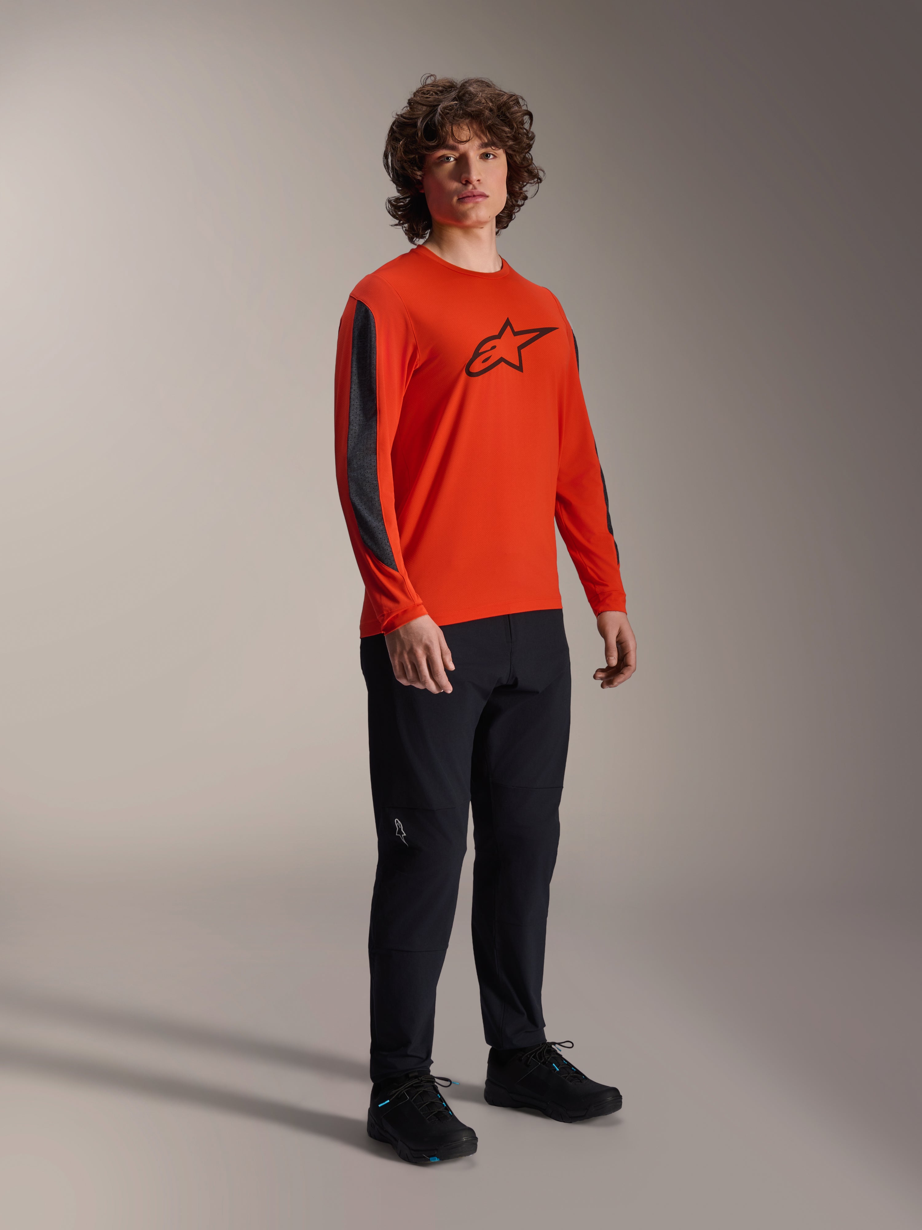 Mannequin homme portant le maillot Alpinestars A-Dura Insert Astar à manches longues, Spicy Orange avec logo Astar noir sur la poitrine et inserts gris foncé sur les manches, porté avec un pantalon noir, équipement de cyclisme VTT professionnel