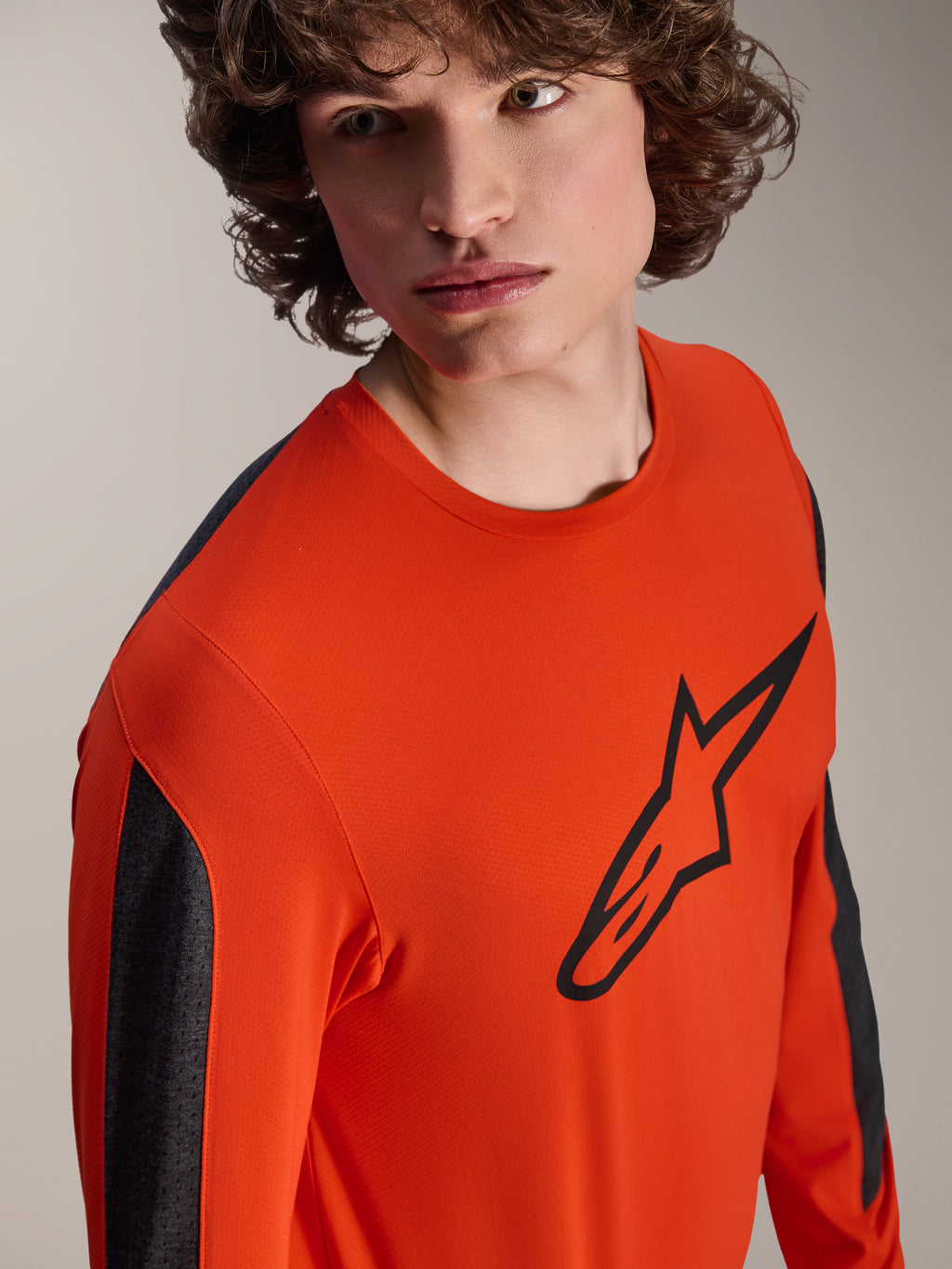 Maillot à manches longues Alpinestars A-Dura Insert Astar, maillot de VTT orange Spicy Orange avec un grand logo Astar noir sur la poitrine, empiècements gris foncé sur les manches, porté par un mannequin en gros plan en studio, tissu technique texturé.