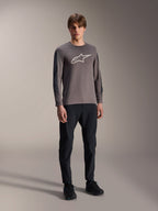 Maillot Alpinestars A-Dura Insert Astar, maillot de VTT à manches longues, gris foncé, avec un grand logo blanc sur la poitrine, porté avec un pantalon technique noir et des chaussures noires, équipement de cyclisme tout-terrain