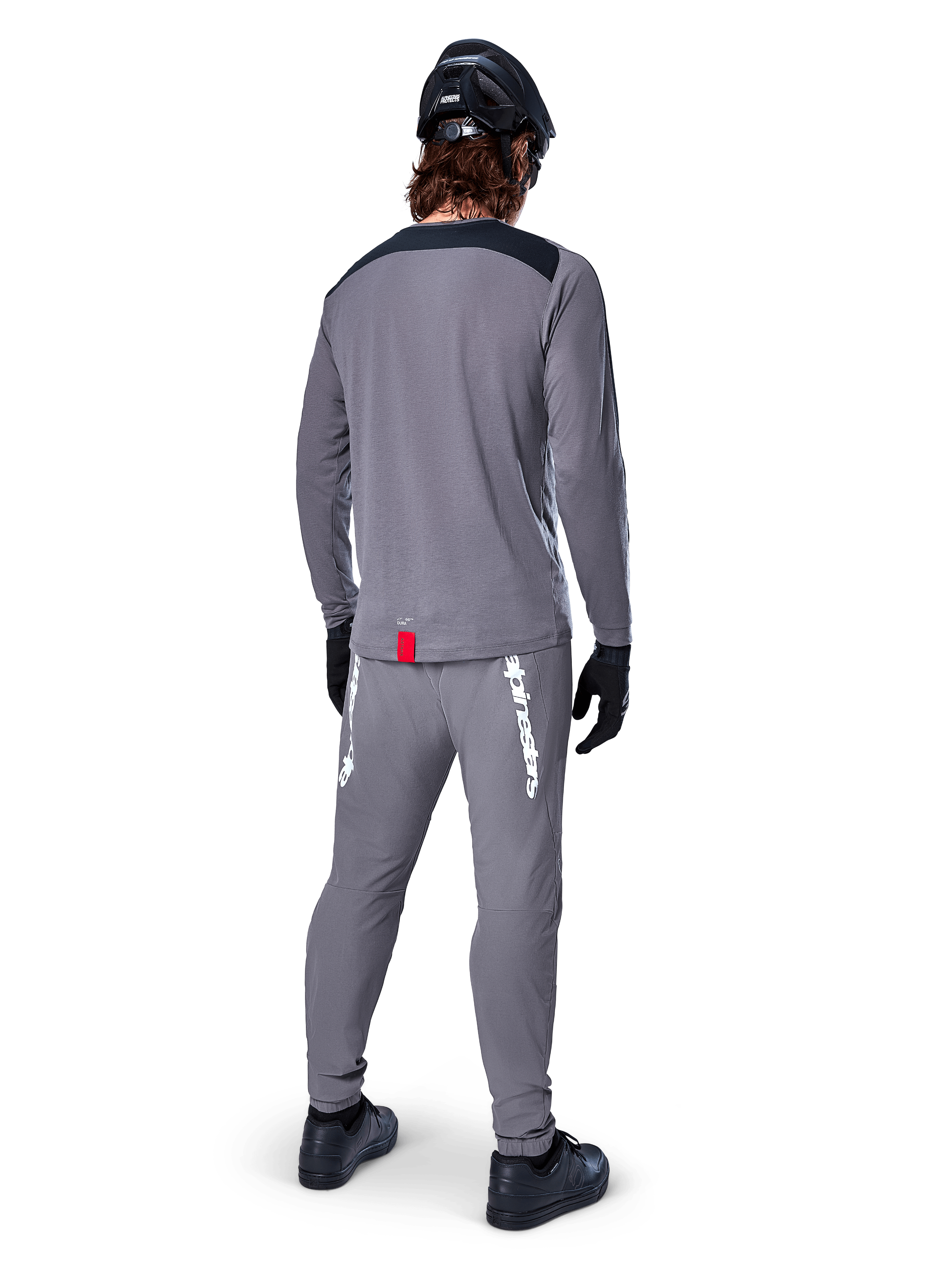 Alpinestars A-Dura Dri Astar Jersey - Long Sleeve, Dark Gray, back view of rider wearing matching pants and black helmet, features black shoulder panels and a small red tag at the hem, technical off-road cycling gear