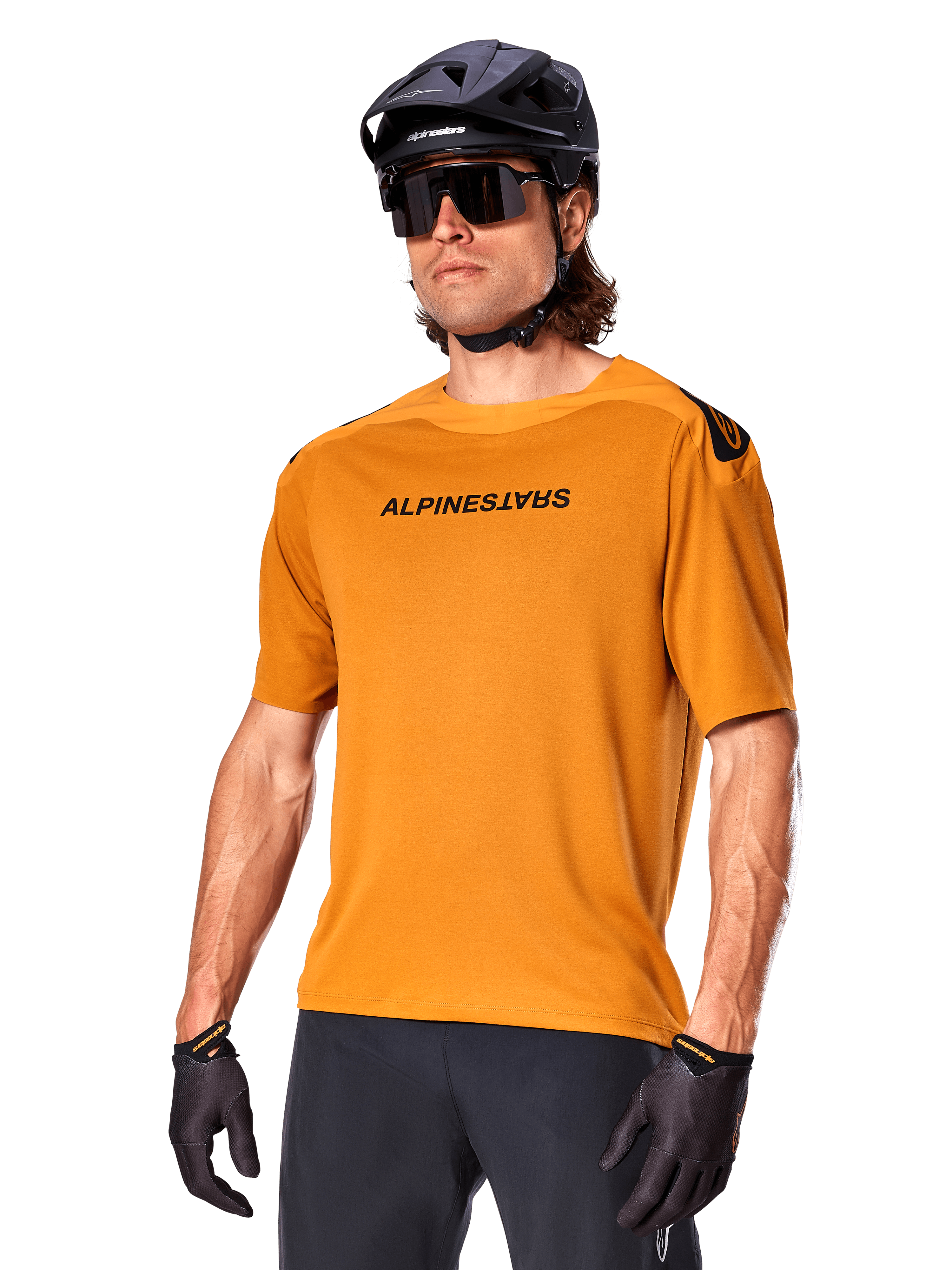 Maillot Alpinestars A-Aria Polartec Switch, maillot de VTT à manches courtes, or foncé avec marquage noir, porté par un mannequin avec casque noir, lunettes de soleil et gants de cyclisme, vêtement de VTT haute performance