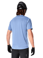 Alpinestars A-Dura Dri Astar Short Sleeve Jersey, MTB Jersey, Infinity Blue, back view showing mesh ventilation panels on shoulders and a longer drop tail, worn with a black MTB helmet and gloves, performance cycling gear