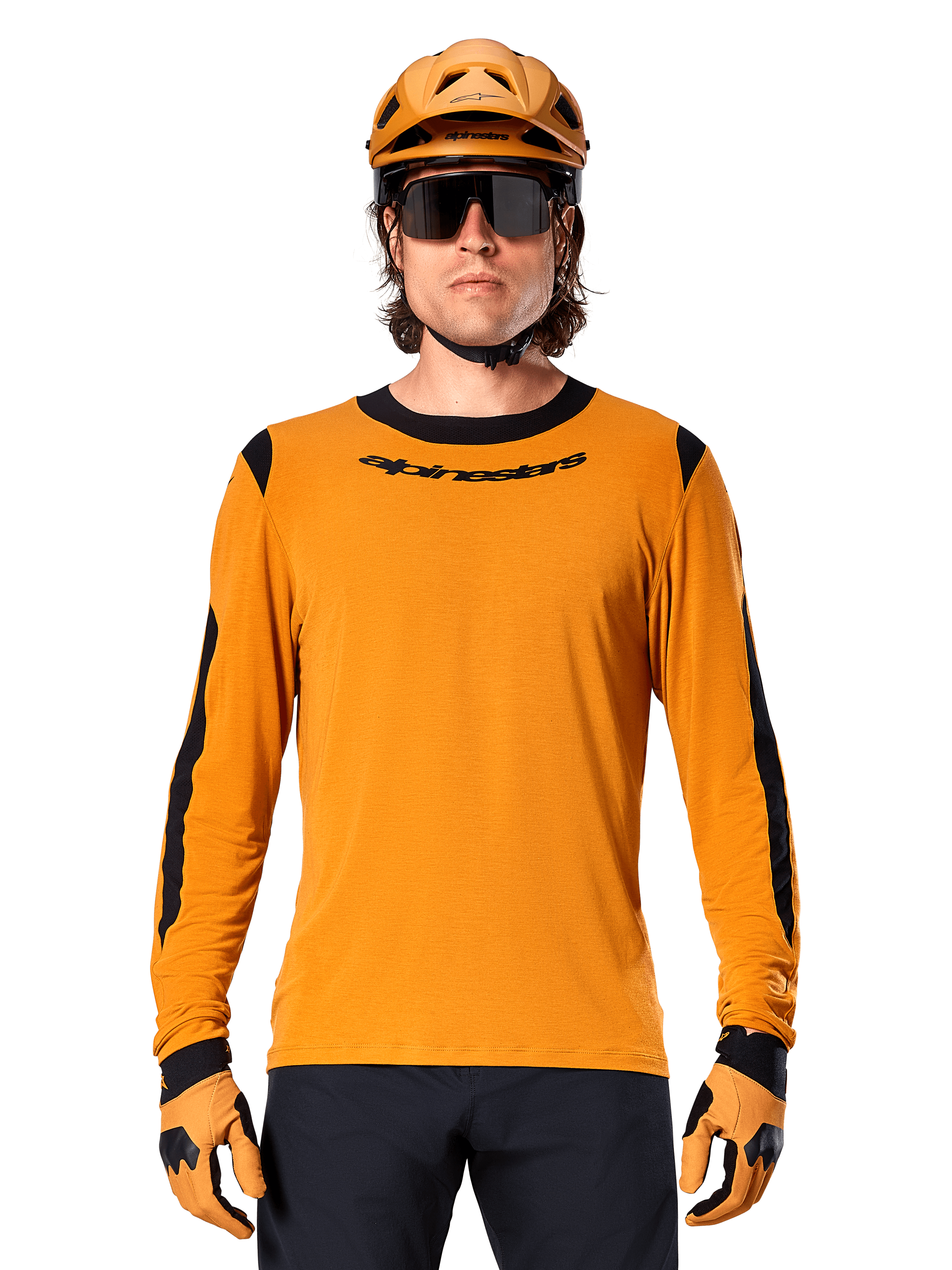 Male model wearing Alpinestars A-Dura Dri Wool Long Sleeve Jersey in Dark Gold, coordinated with a matching gold MTB helmet and gloves, black mesh panels on shoulders and sleeves, black Alpinestars wordmark on chest, dark sunglasses and pants, technical mountain bike apparel