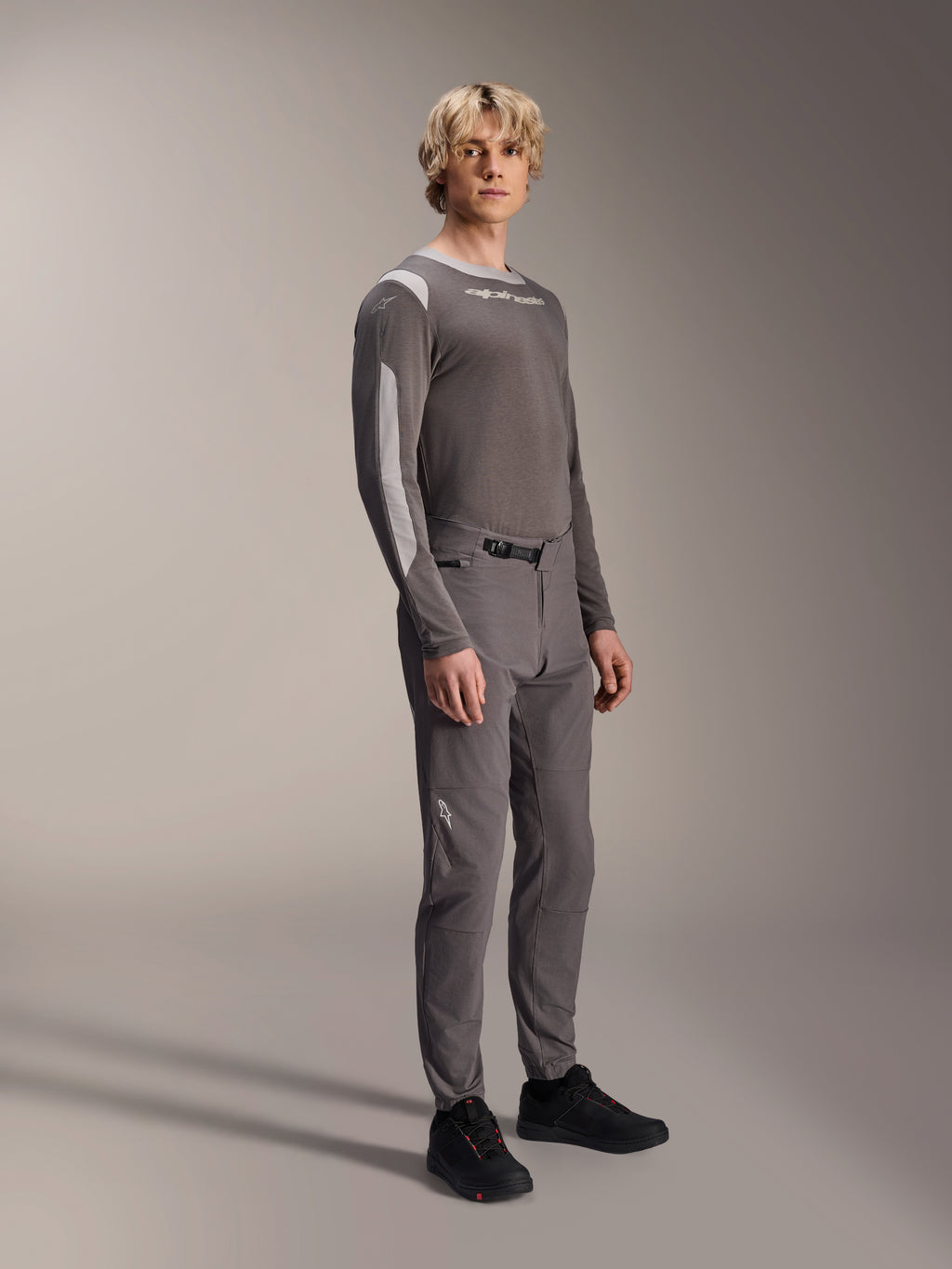 Pantalon Alpinestars A-Dura Elite, pantalon de VTT, gris foncé, porté avec un maillot à manches longues assorti et des chaussures noires, doté d'une fermeture à cliquet à l'avant et d'un tissu Cordura durable pour le trail et l'enduro
