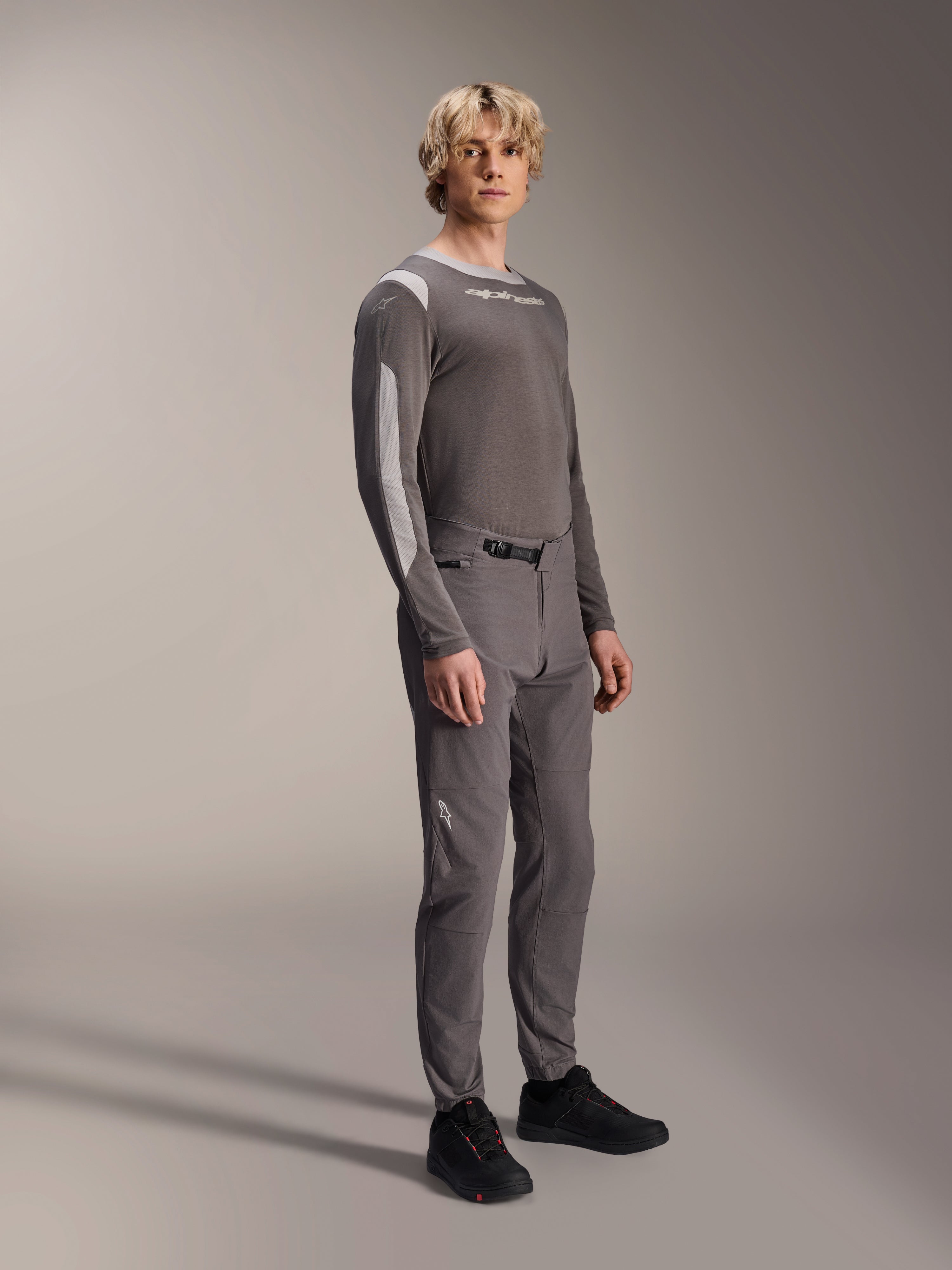 Pantalon Alpinestars A-Dura Elite, pantalon de VTT, gris foncé, porté avec un maillot à manches longues assorti et des chaussures noires, doté d'une fermeture à cliquet à l'avant et d'un tissu Cordura durable pour le trail et l'enduro