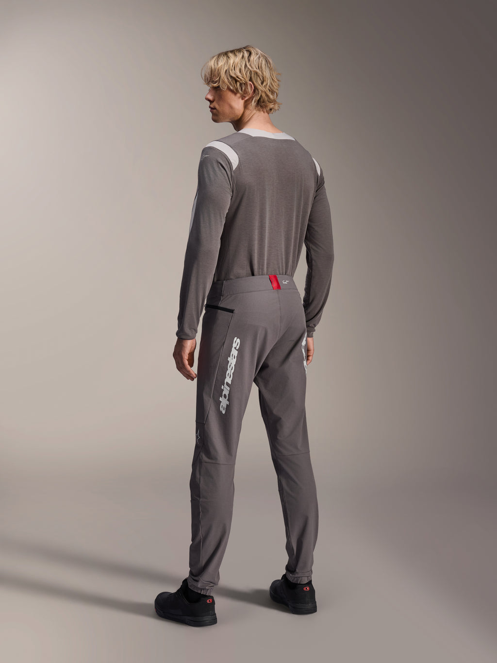 Modèle vu de dos portant un équipement de VTT Alpinestars, maillot à manches longues gris A-Dura Dri Wool, pantalon A-Dura Elite gris foncé avec marquage vertical blanc et détail rouge à la taille, tenue de cyclisme coordonnée pour le VTT