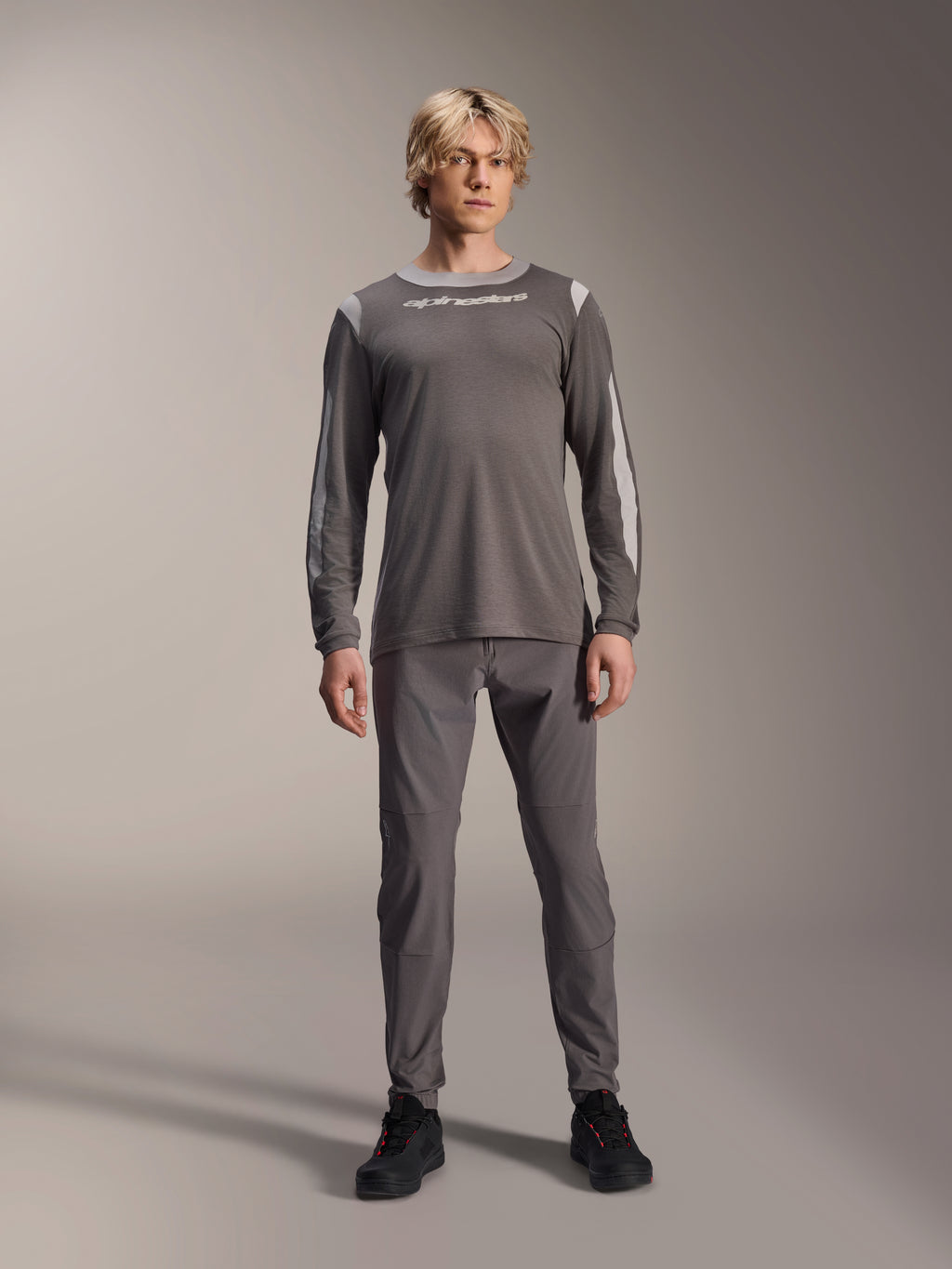 Maillot à manches longues Alpinestars A-Dura Dri Wool, gris foncé, porté par un mannequin avec un pantalon gris assorti et des chaussures noires, logo Alpinestars blanc sur la poitrine, panneaux en maille gris clair sur les épaules et les manches, équipement technique de VTT