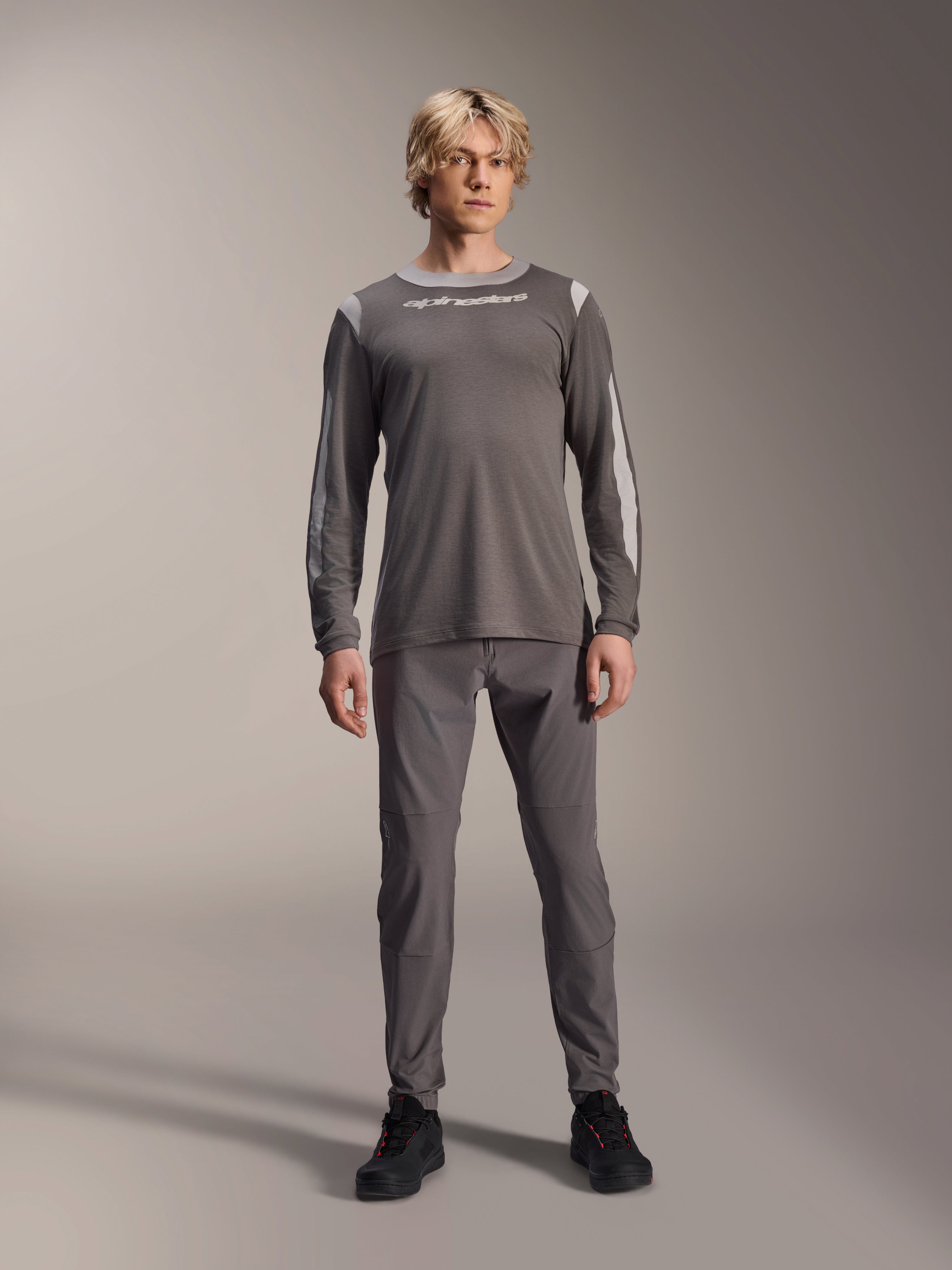 Maillot à manches longues Alpinestars A-Dura Dri Wool, gris foncé, porté par un mannequin avec un pantalon gris assorti et des chaussures noires, logo Alpinestars blanc sur la poitrine, panneaux en maille gris clair sur les épaules et les manches, équipement technique de VTT