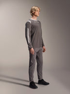 Modèle masculin portant le maillot à manches longues Alpinestars A-Dura Dri Wool en gris foncé, associé à un pantalon gris assorti et des chaussures noires, avec des panneaux en maille gris clair sur les épaules et les manches, équipement technique de VTT pour le cyclisme tout-terrain