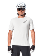 Cyclist wearing Alpinestars A-Aria Astar Short Sleeve Jersey, White Dove with small black Astar logo on chest, white cycling helmet, black sunglasses, and black and white gloves, performance MTB gear for off-road riding