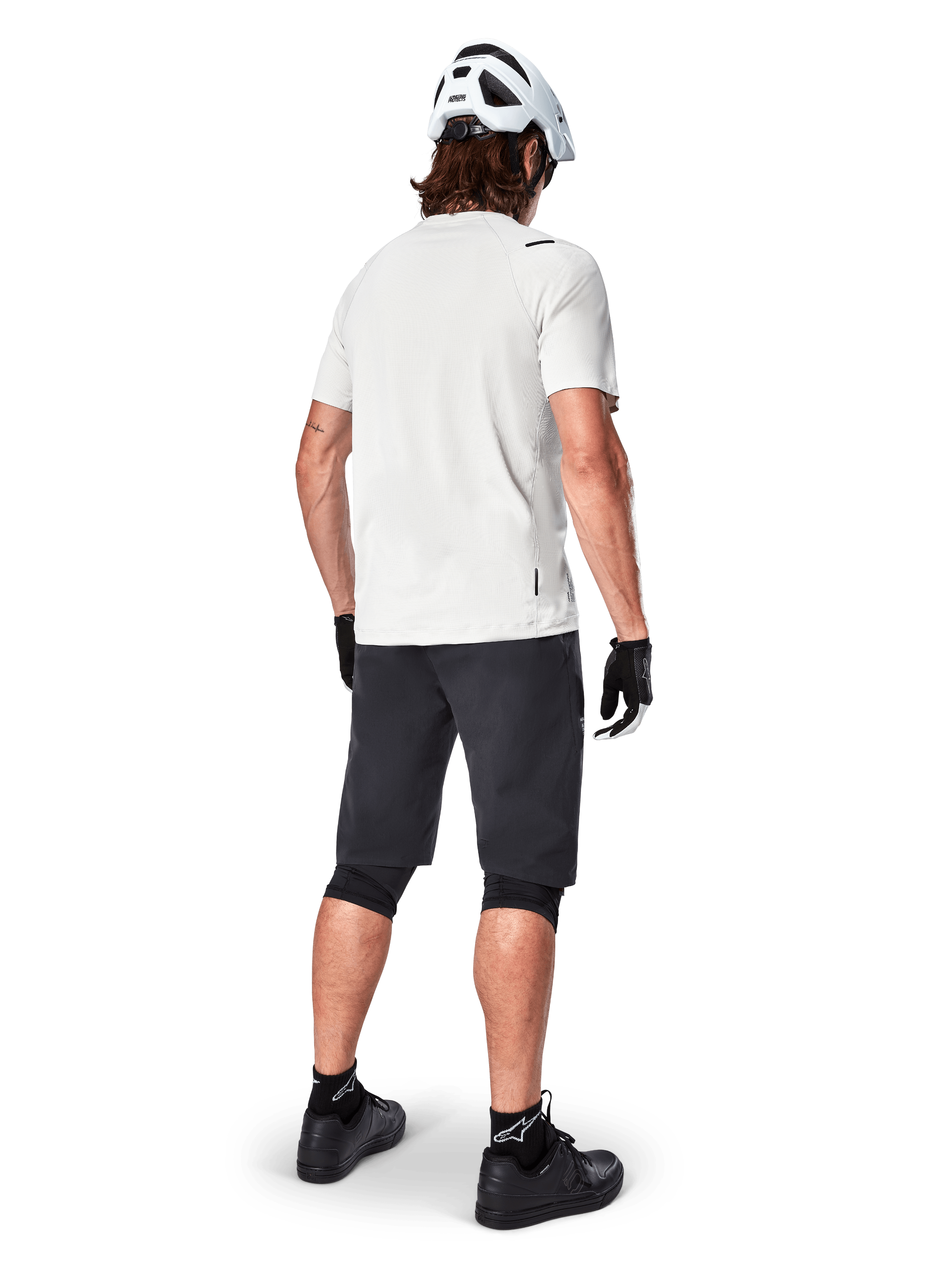 Cyclist wearing the Alpinestars A-Aria Astar Short Sleeve Jersey in White Dove, rear view, paired with black MTB shorts, knee guards, and a white helmet, lightweight and breathable gear for off-road mountain biking
