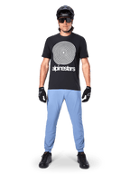 Alpinestars A-Dura Oscar Jersey - Short Sleeve, Black MTB Jersey, featuring a large white vintage Oscar spiral graphic and brand text, worn with light blue pants, black helmet, sunglasses, and black gloves, performance mountain bike apparel