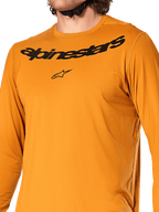 Alpinestars A-Dura Rocker Long Sleeve Jersey, Dark Gold, close-up view of chest featuring black Alpinestars wordmark and star logo, textured jacquard moisture-wicking fabric, performance MTB cycling apparel