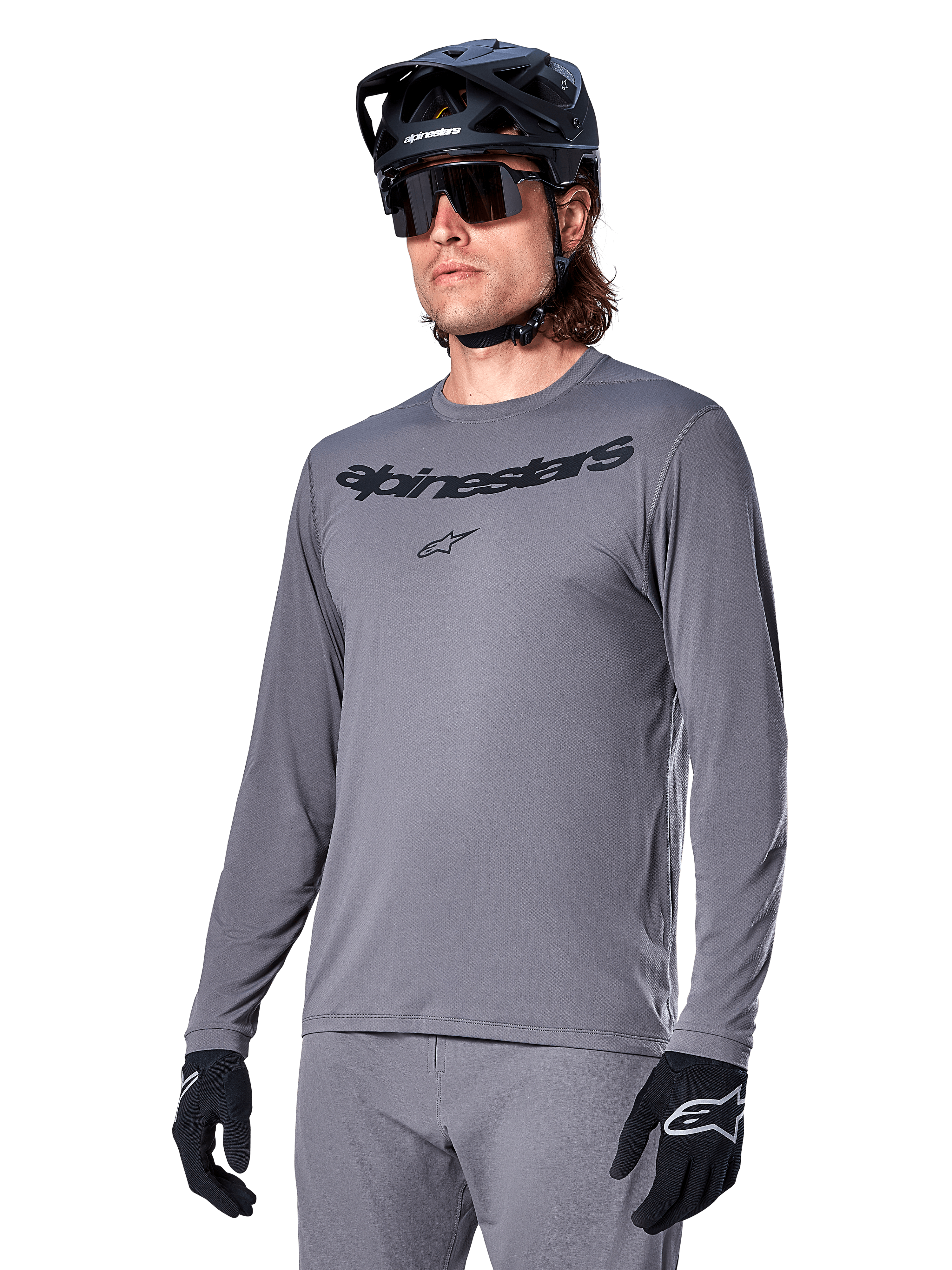 Maillot à manches longues Alpinestars A-Dura Rocker, maillot de VTT gris, porté avec casque et gants noirs, logo noir sur la poitrine, tenue de cyclisme sportive pour le tout-terrain, fond uni