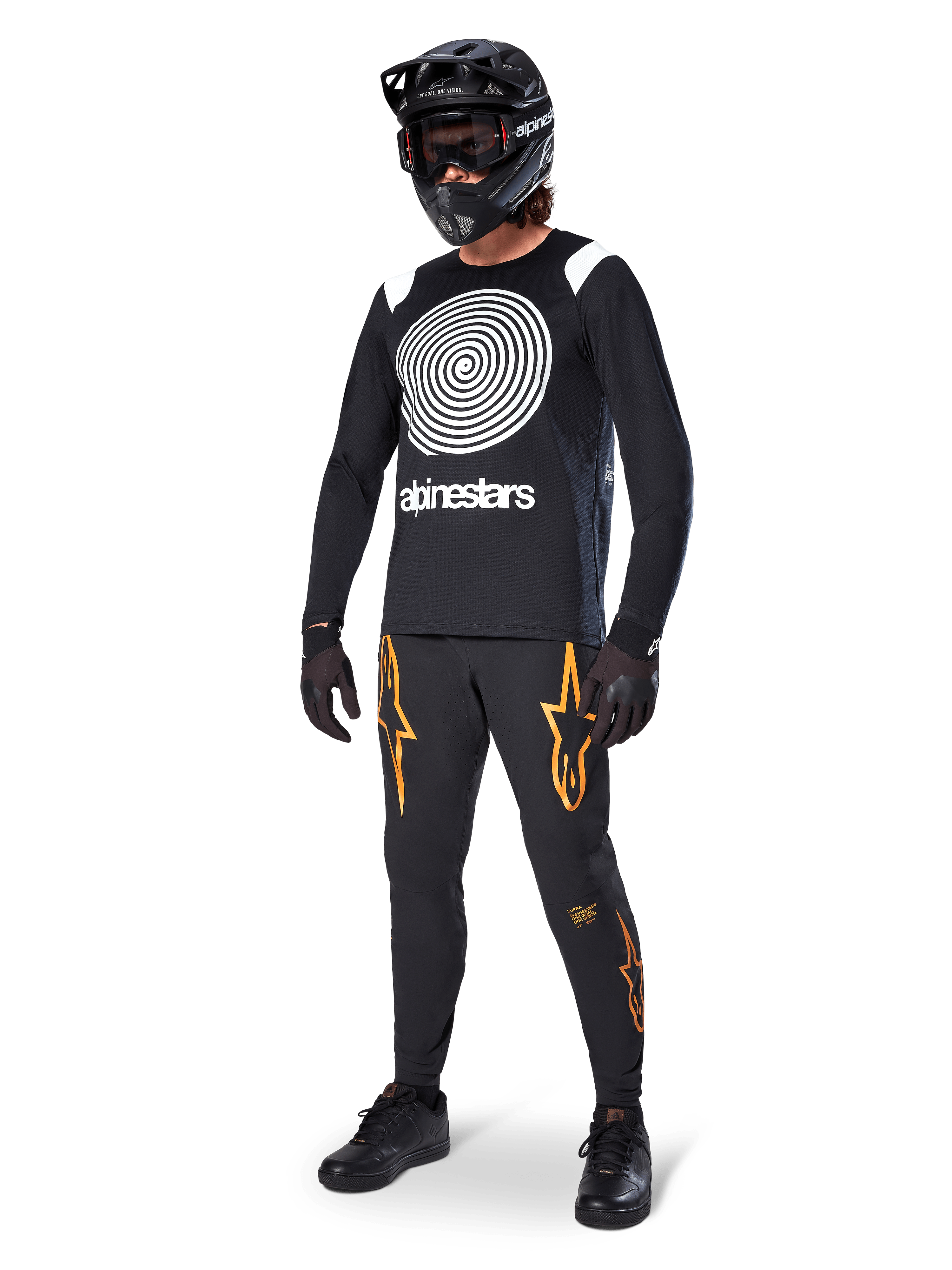 MTB rider wearing Alpinestars A-Supra Oscar Long Sleeve Jersey in Black, featuring the white vintage Oscar spiral graphic, black pants with orange star logos, black full-face helmet with goggles, and black gloves, professional mountain biking gear
