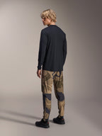 Alpinestars A-Dura Camo Pant, pantalon de VTT, camouflage brun, porté avec un maillot à manches longues noir et des baskets noires, vue arrière montrant des jambes fuselées et des chevilles élastiquées, vêtement de performance pour le cyclisme tout-terrain