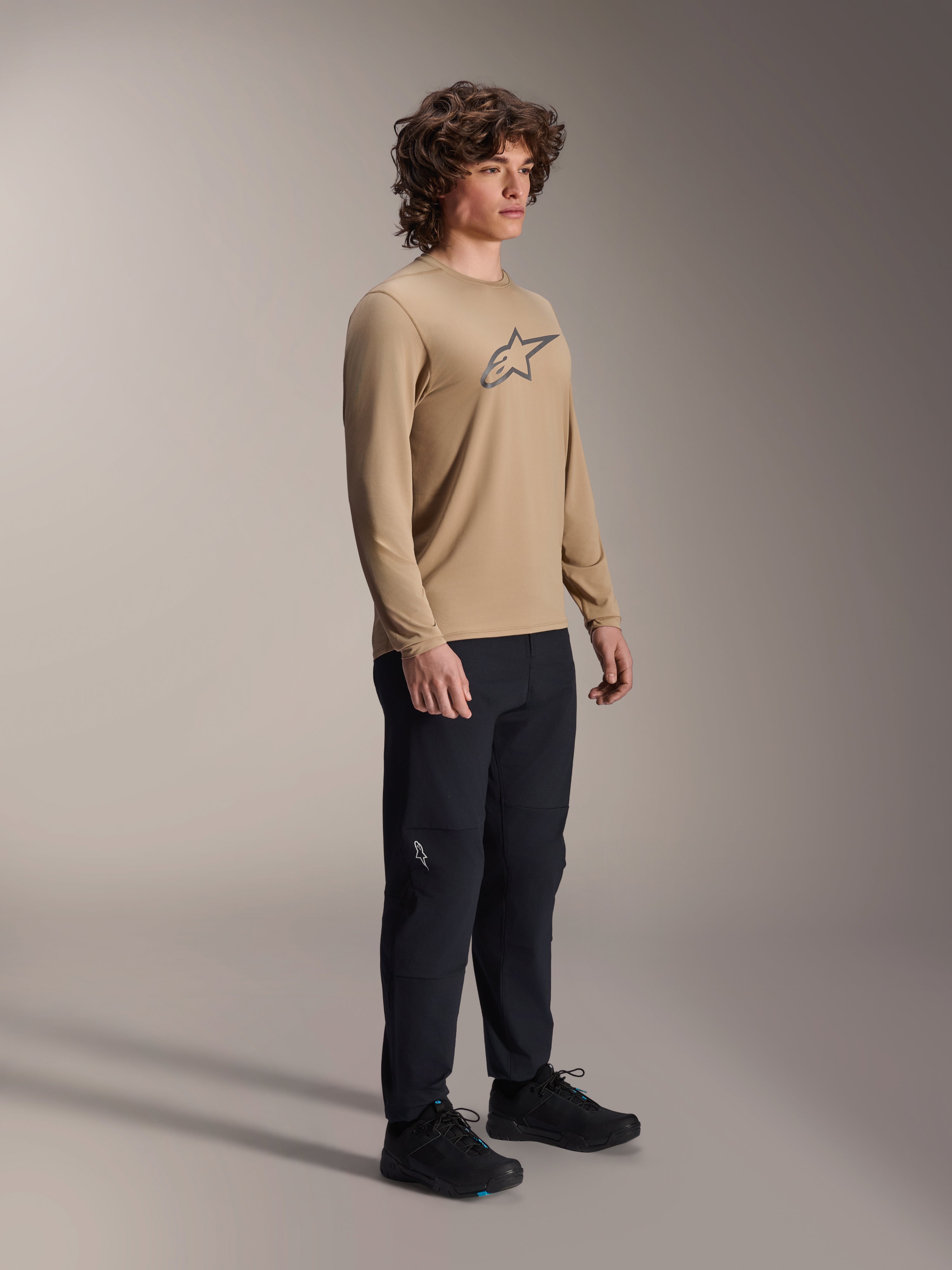 Maillot à manches longues Alpinestars A-Dura Astar, brun clair, porté par un mannequin avec un pantalon et des chaussures noirs, arborant un logo Astars gris sur la poitrine, équipement de performance décontracté pour le VTT