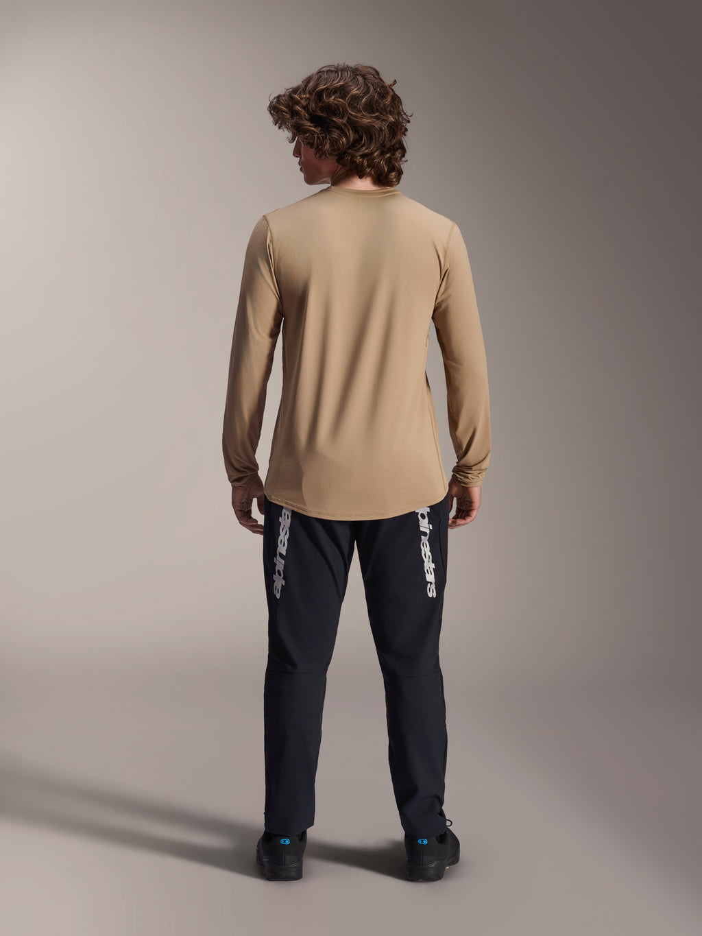 Maillot à manches longues Alpinestars A-Dura Astar, Brun clair, vue de dos montrant le pan arrière plus long, porté avec un pantalon noir arborant le logo Alpinestars, équipement de VTT haute performance