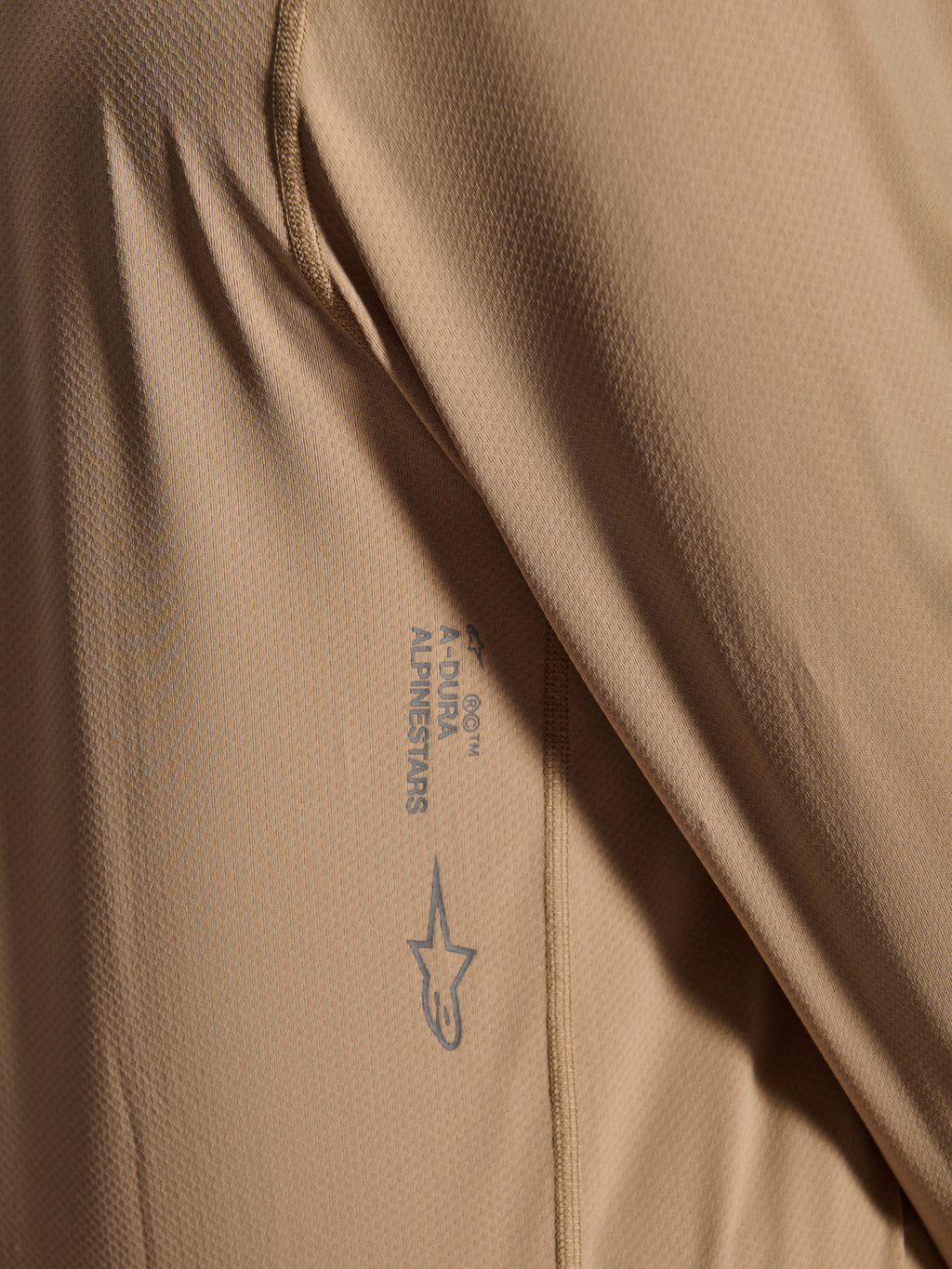 Maillot à manches longues Alpinestars A-Dura Astar, maillot de cyclisme VTT, brun, gros plan montrant la texture du tissu jacquard, logo Astars et mot-symbole A-Dura imprimés, vêtement technique de VTT
