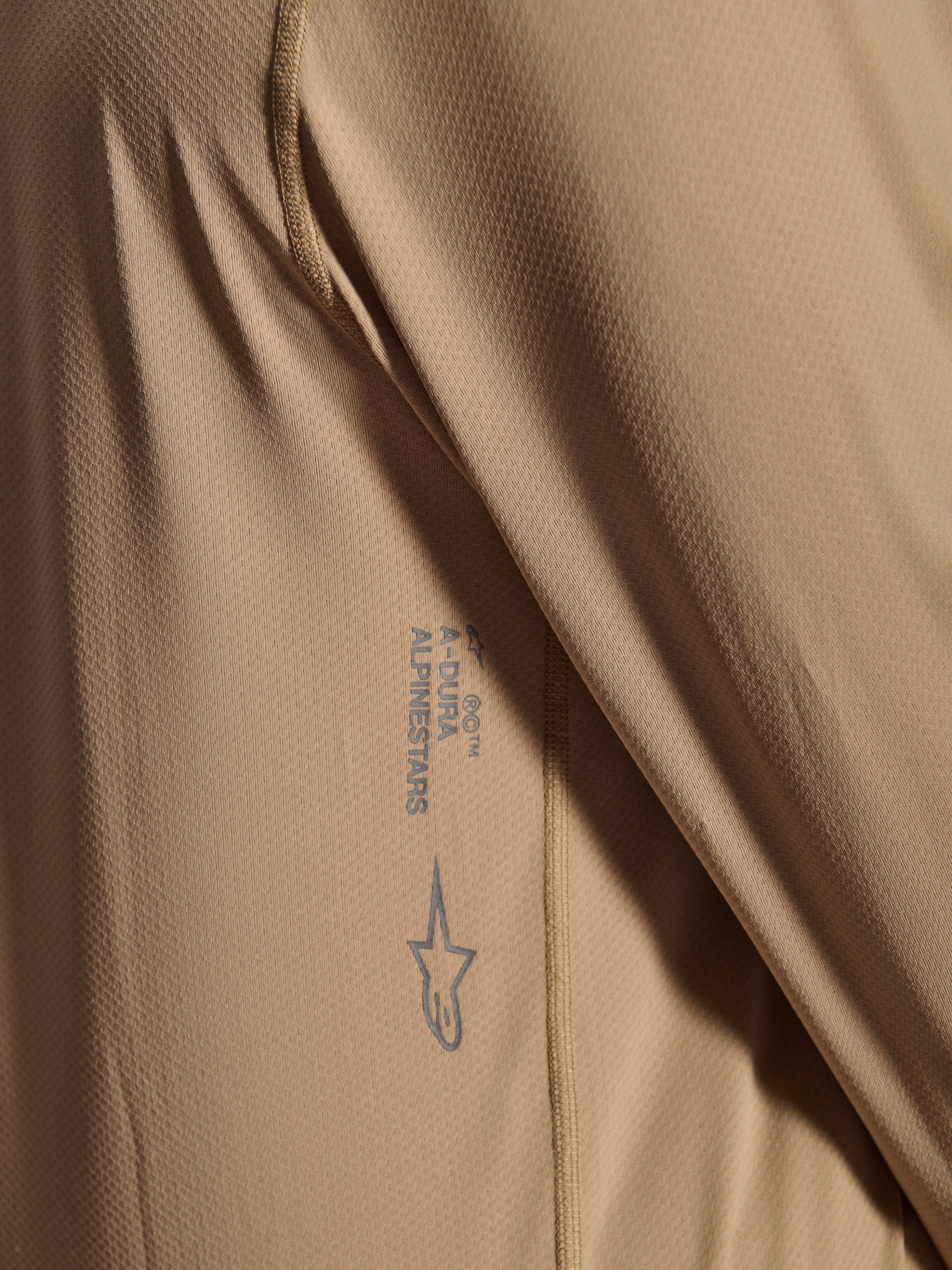 Maillot à manches longues Alpinestars A-Dura Astar, maillot de cyclisme VTT, brun, gros plan montrant la texture du tissu jacquard, logo Astars et mot-symbole A-Dura imprimés, vêtement technique de VTT