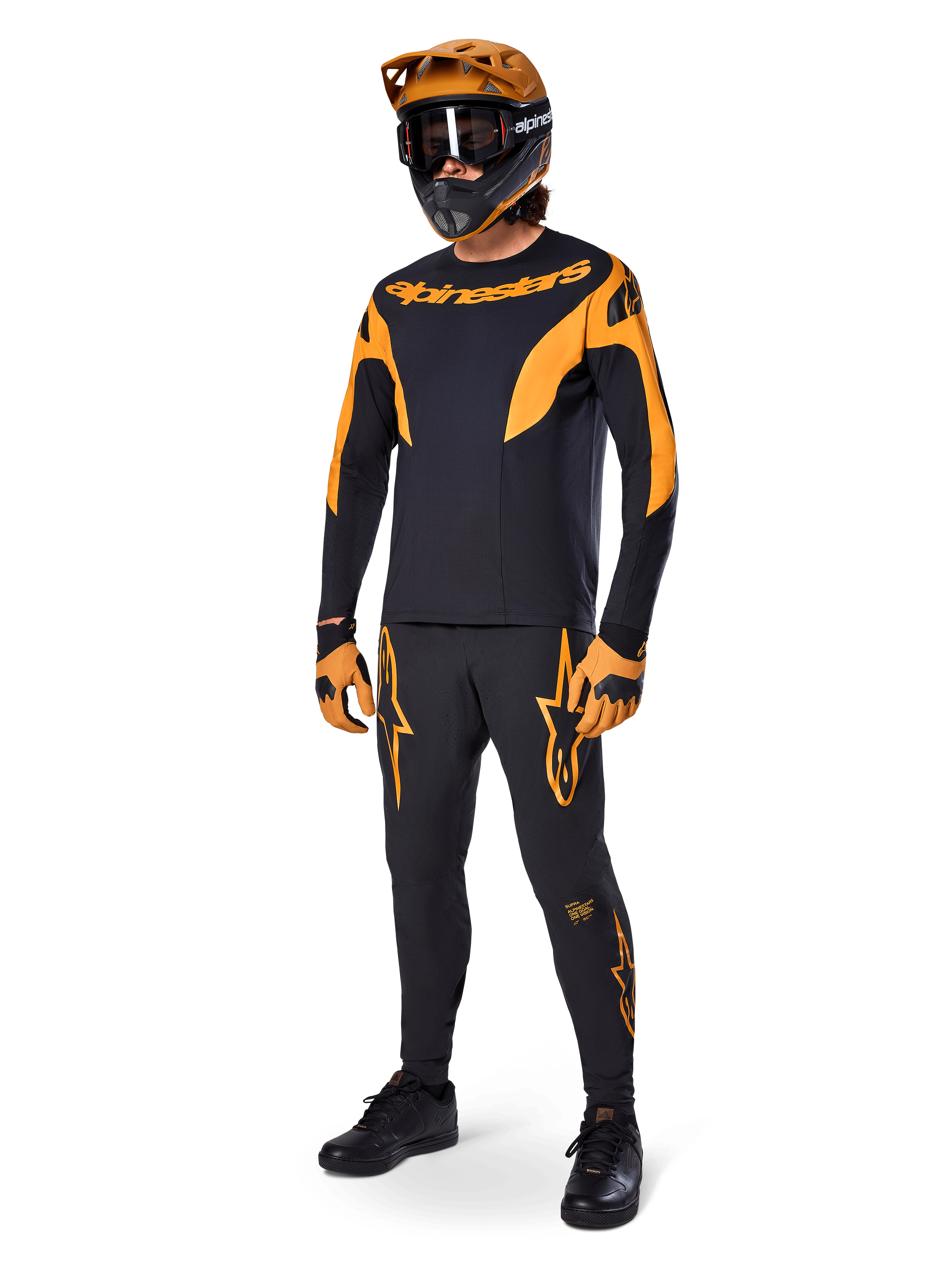 MTB rider wearing complete racing gear, Black A-Supra Race Jersey with orange accents, matching black pants with orange Alpinestars logos, orange and black full-face helmet with goggles, orange and black gloves, coordinated outfit for mountain bike racing