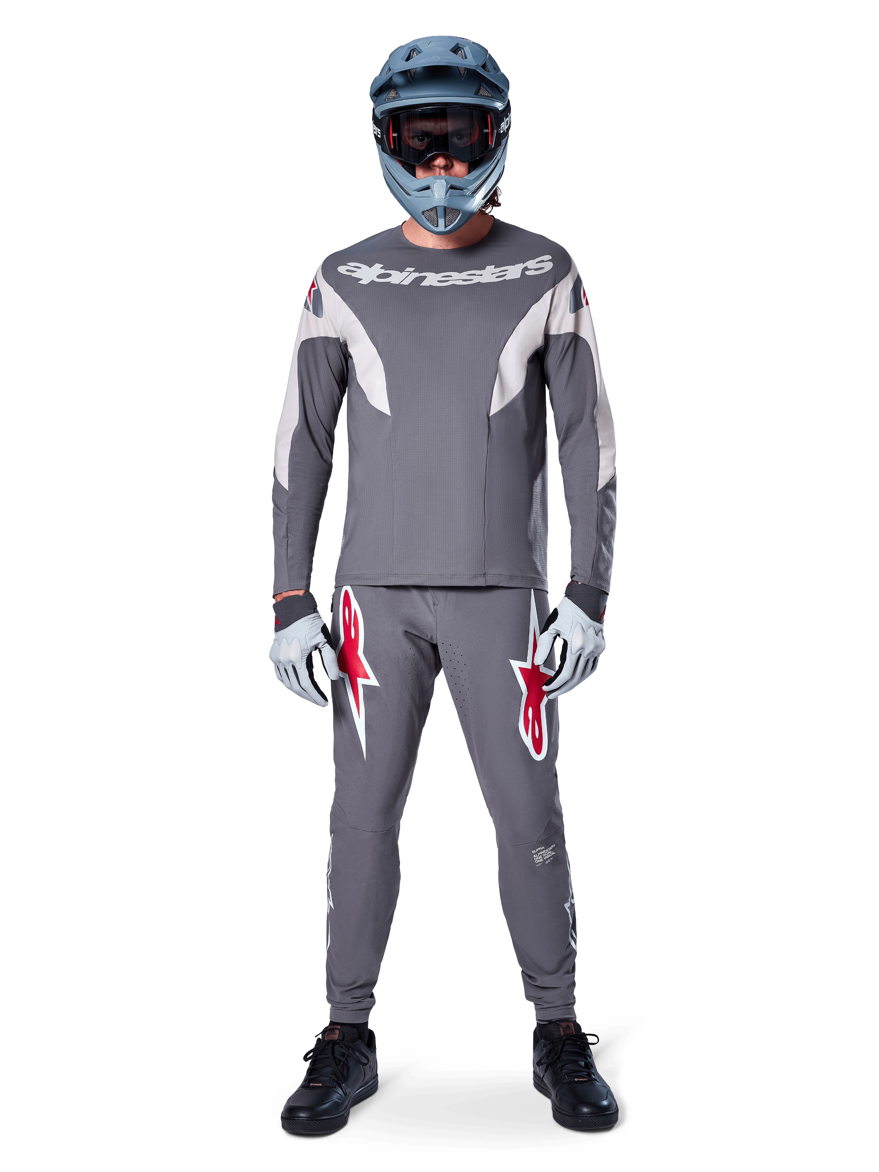Pilote portant le maillot Alpinestars A-Supra Race - Manches longues en gris foncé, coordonné avec un pantalon gris assorti arborant des logos d'étoiles rouges, un casque gris avec lunettes et des gants gris clair, kit de VTT complet pour le cyclisme tout-terrain de performance