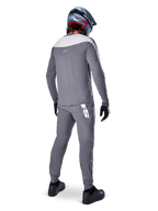 Maillot Alpinestars A-Supra Race, maillot de VTT à manches longues, gris foncé avec empiècement gris clair sur les épaules, vue de dos porté avec un pantalon assorti, casque intégral bleu et rouge, gants et chaussures noirs, équipement de cyclisme de performance inspiré par la course