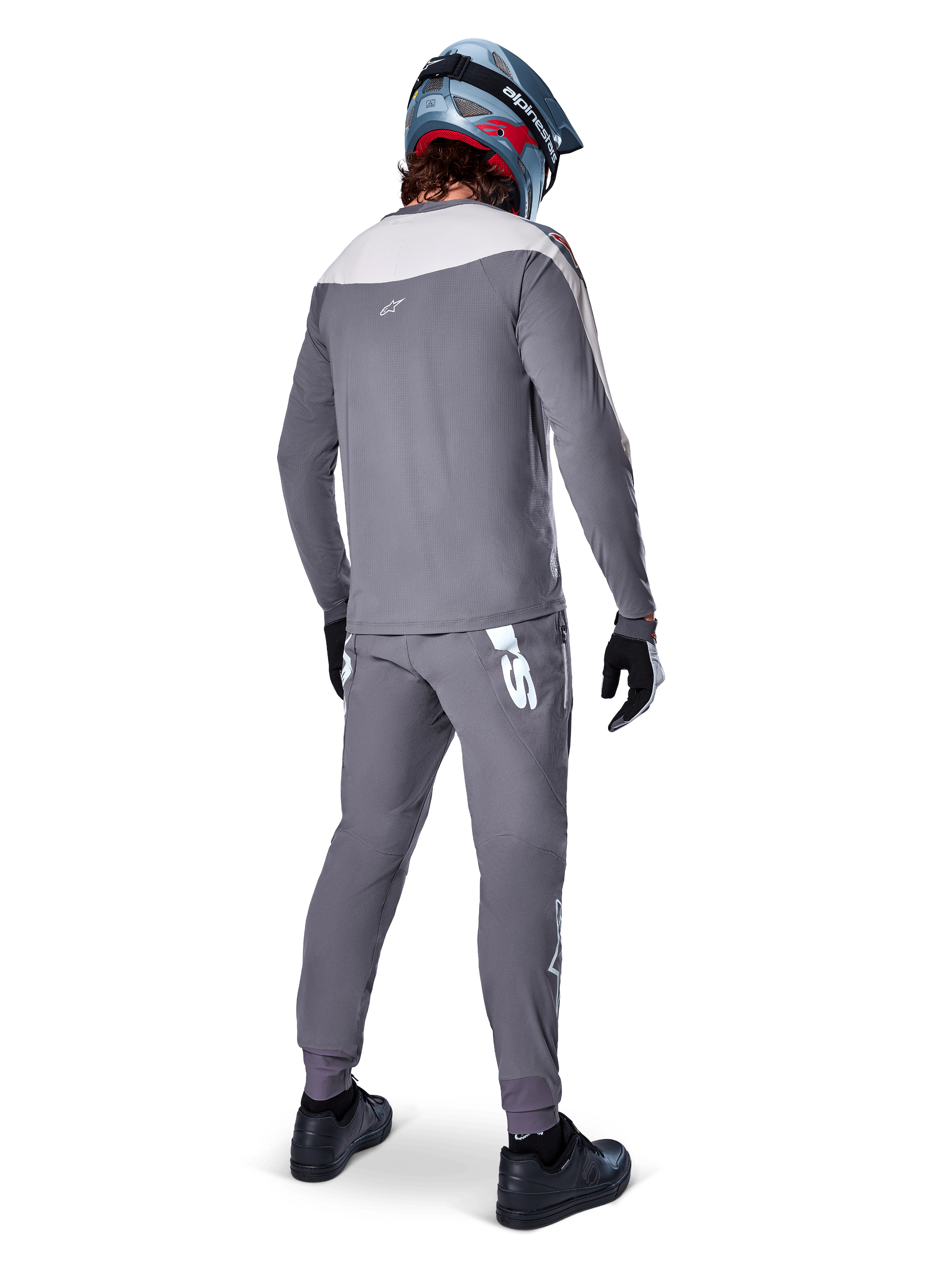 Maillot Alpinestars A-Supra Race, maillot de VTT à manches longues, gris foncé avec empiècement gris clair sur les épaules, vue de dos porté avec un pantalon assorti, casque intégral bleu et rouge, gants et chaussures noirs, équipement de cyclisme de performance inspiré par la course