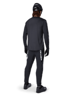 Alpinestars A-Dura Switch Long Sleeve Jersey, Black, rear view on a rider, worn with black pants featuring white Alpinestars branding, black helmet, and gloves, featuring a drop tail for extra coverage, performance mountain bike apparel