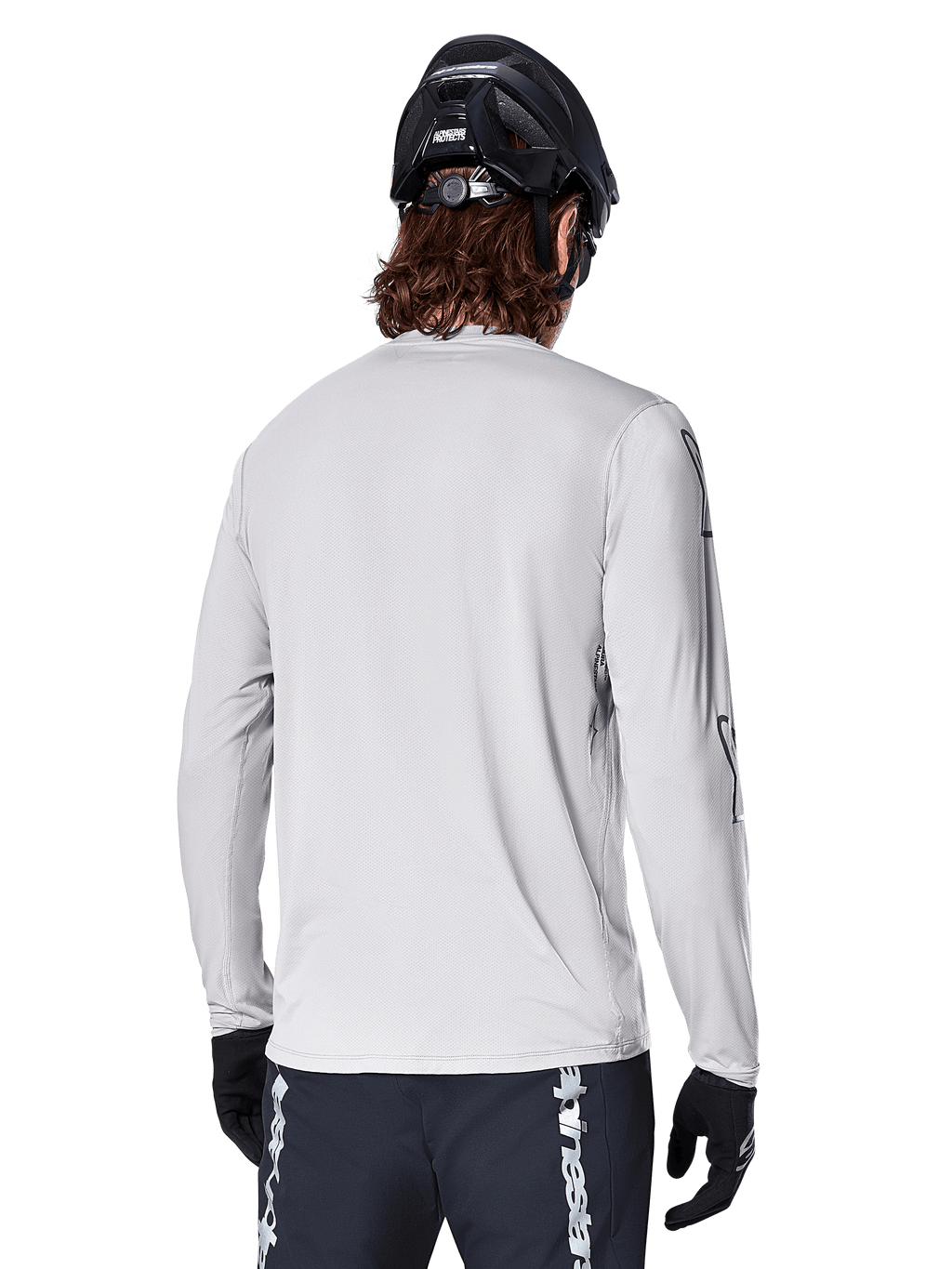 Maillot à manches longues Alpinestars A-Dura Switch, gris clair, vue arrière d'un vététiste portant un casque de VTT noir et des gants, avec une coupe arrière plus longue pour une protection accrue et un tissu jacquard texturé, équipement de cyclisme haute performance