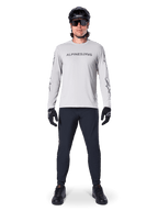 Maillot à manches longues Alpinestars A-Dura Switch en gris clair, avec un logo textuel stylisé sur la poitrine, porté avec un pantalon noir, un casque et des gants, vêtement de VTT haute performance pour le cyclisme tout-terrain