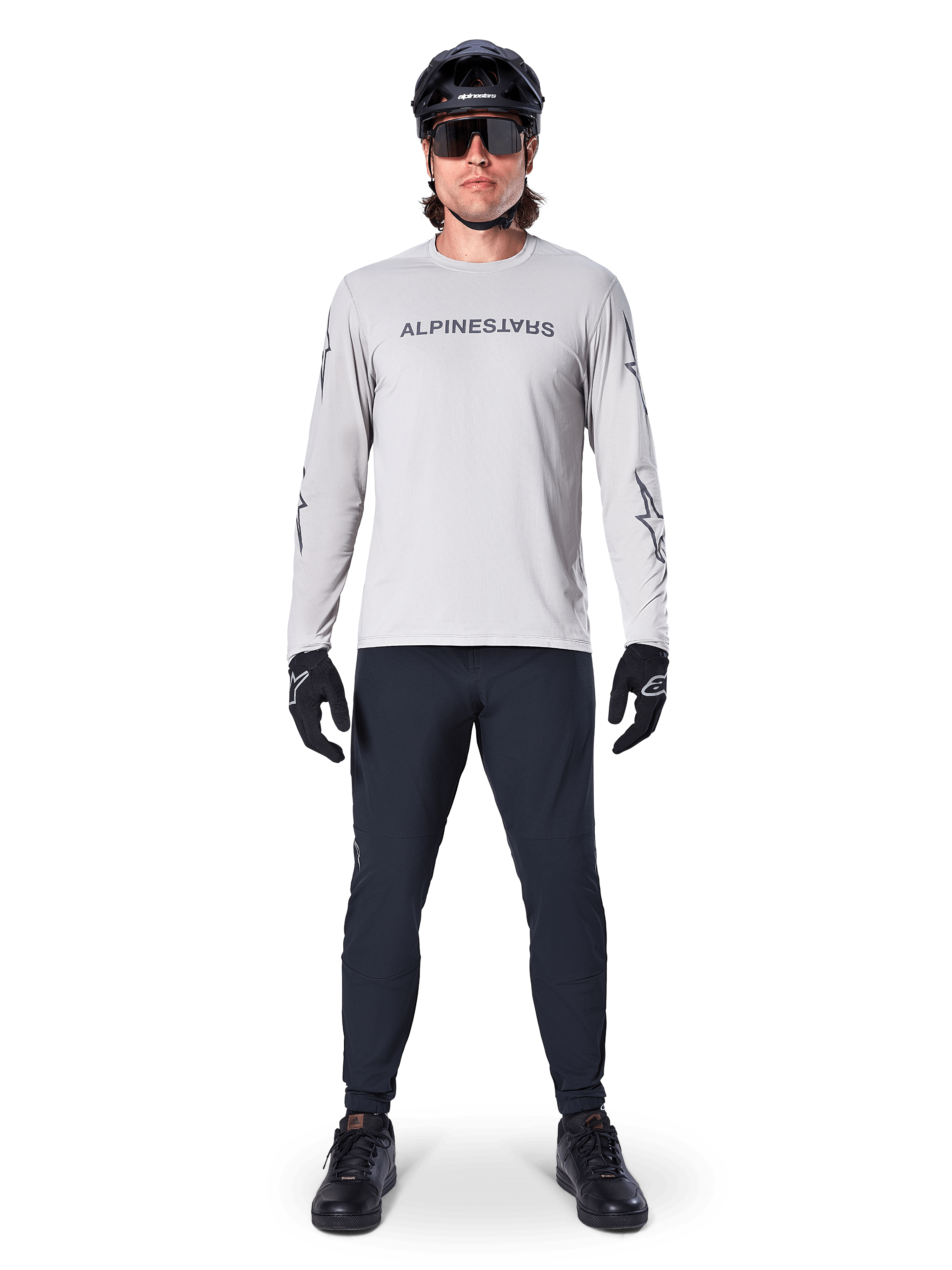 Maillot à manches longues Alpinestars A-Dura Switch en gris clair, avec un logo textuel stylisé sur la poitrine, porté avec un pantalon noir, un casque et des gants, vêtement de VTT haute performance pour le cyclisme tout-terrain