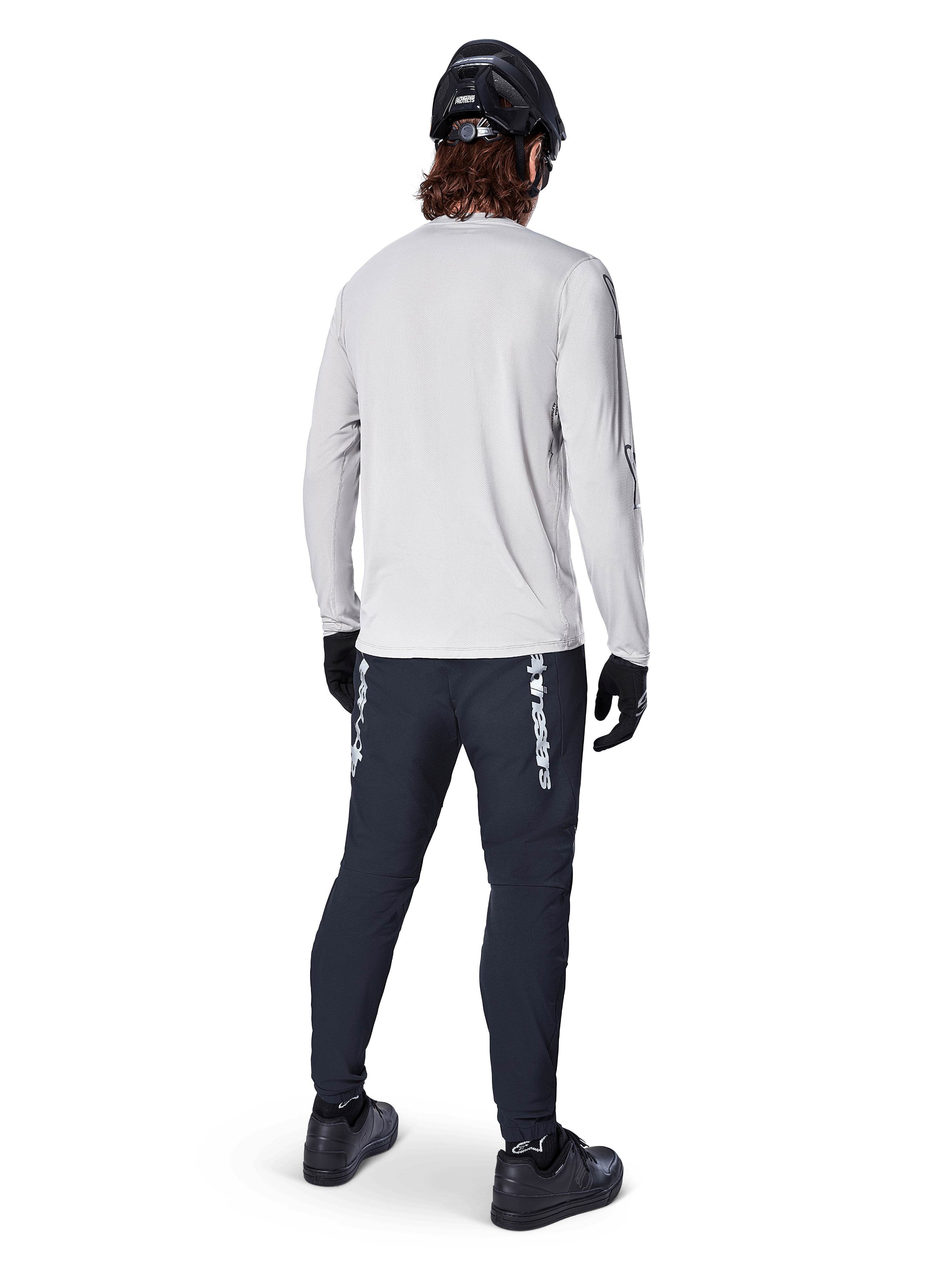 Maillot à manches longues Alpinestars A-Dura Switch, gris clair, vue arrière d'un cycliste portant un pantalon de cyclisme noir, un casque et des gants, équipement de VTT haute performance avec une queue plus longue.