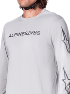 Maillot à manches longues Alpinestars A-Dura Switch, maillot de VTT gris clair avec logo textuel gris foncé sur la poitrine et logo étoilé sur la manche, texture jacquard respirante, équipement de cyclisme de performance pour le trail