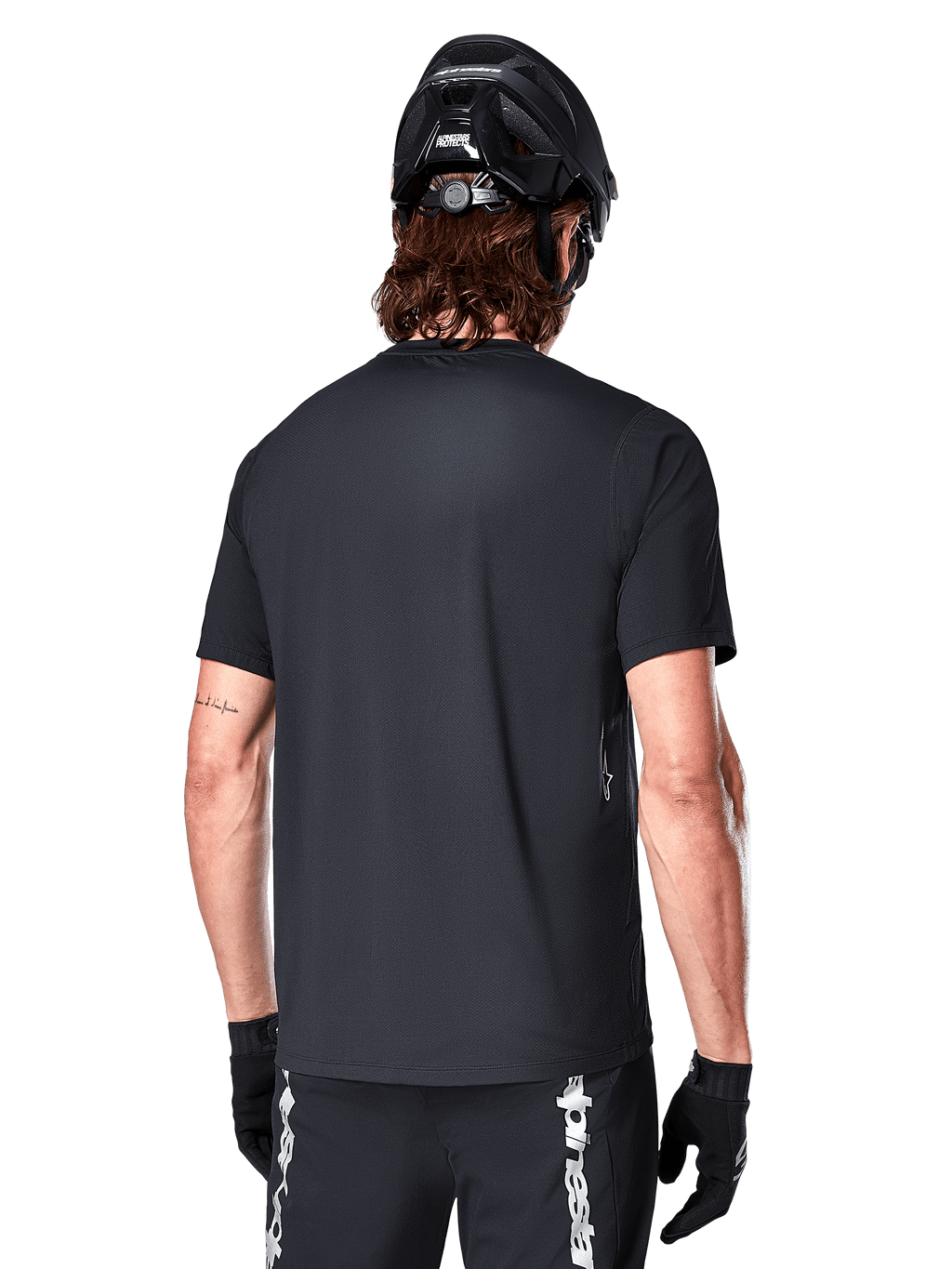 Maillot à manches courtes Alpinestars A-Dura Switch, noir, vue arrière d'un mannequin portant un casque de cyclisme noir et un short de VTT, mettant en avant la coupe régulière et le pan arrière allongé conçu pour le VTT.