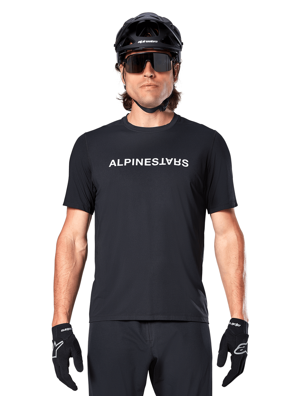 Cycliste de VTT portant le maillot à manches courtes Alpinestars A-Dura Switch noir, avec logo textuel blanc sur la poitrine, casque noir, grandes lunettes de soleil et gants noirs, équipement de cyclisme professionnel pour le trail
