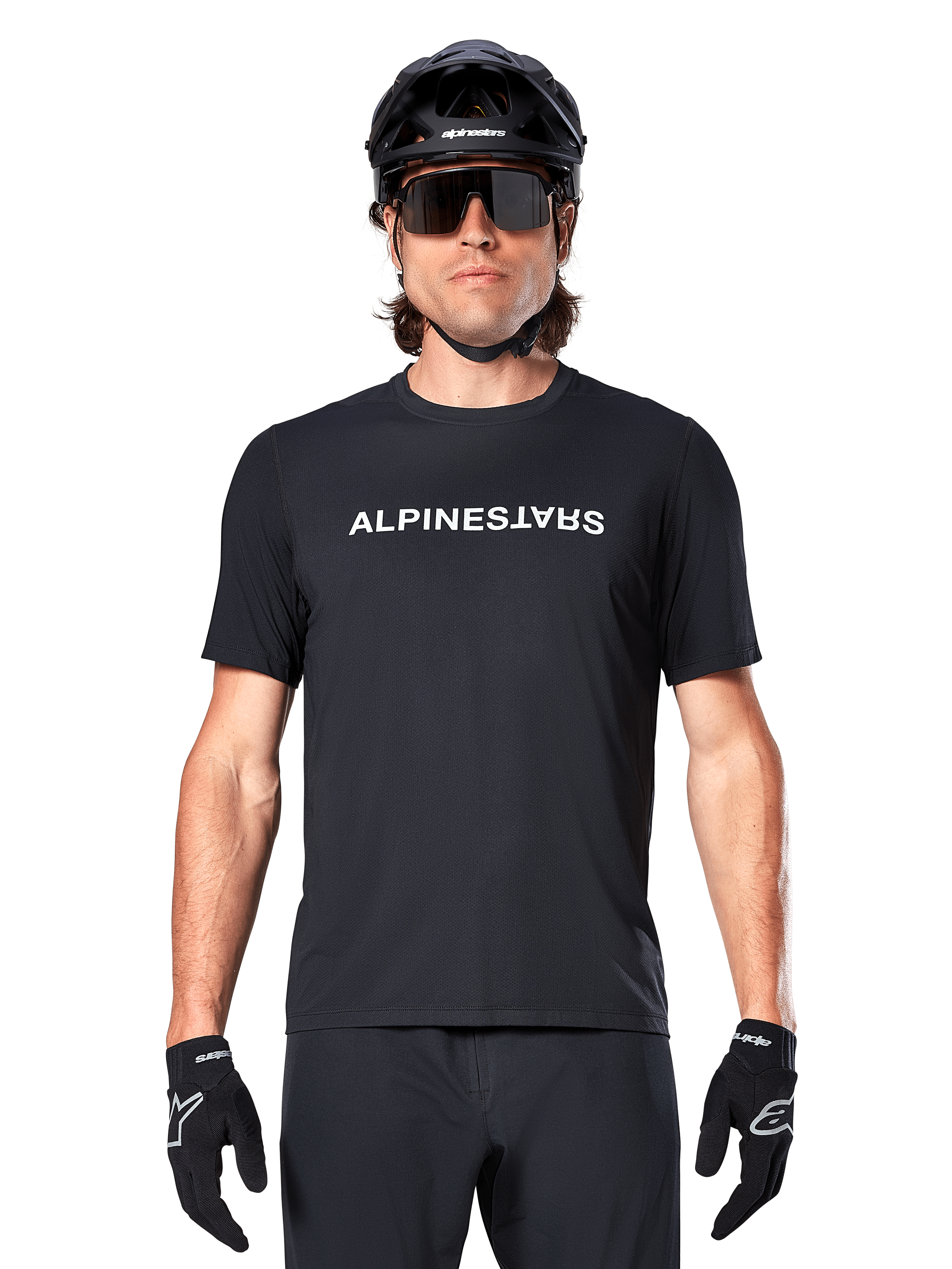 Cycliste de VTT portant le maillot à manches courtes Alpinestars A-Dura Switch noir, avec logo textuel blanc sur la poitrine, casque noir, grandes lunettes de soleil et gants noirs, équipement de cyclisme professionnel pour le trail