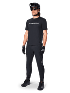 Maillot à manches courtes Alpinestars A-Dura Switch, noir, porté par un mannequin avec pantalon de VTT noir, casque et gants assortis, arborant le logo Alpinestars blanc sur la poitrine, vêtement de performance pour le VTT