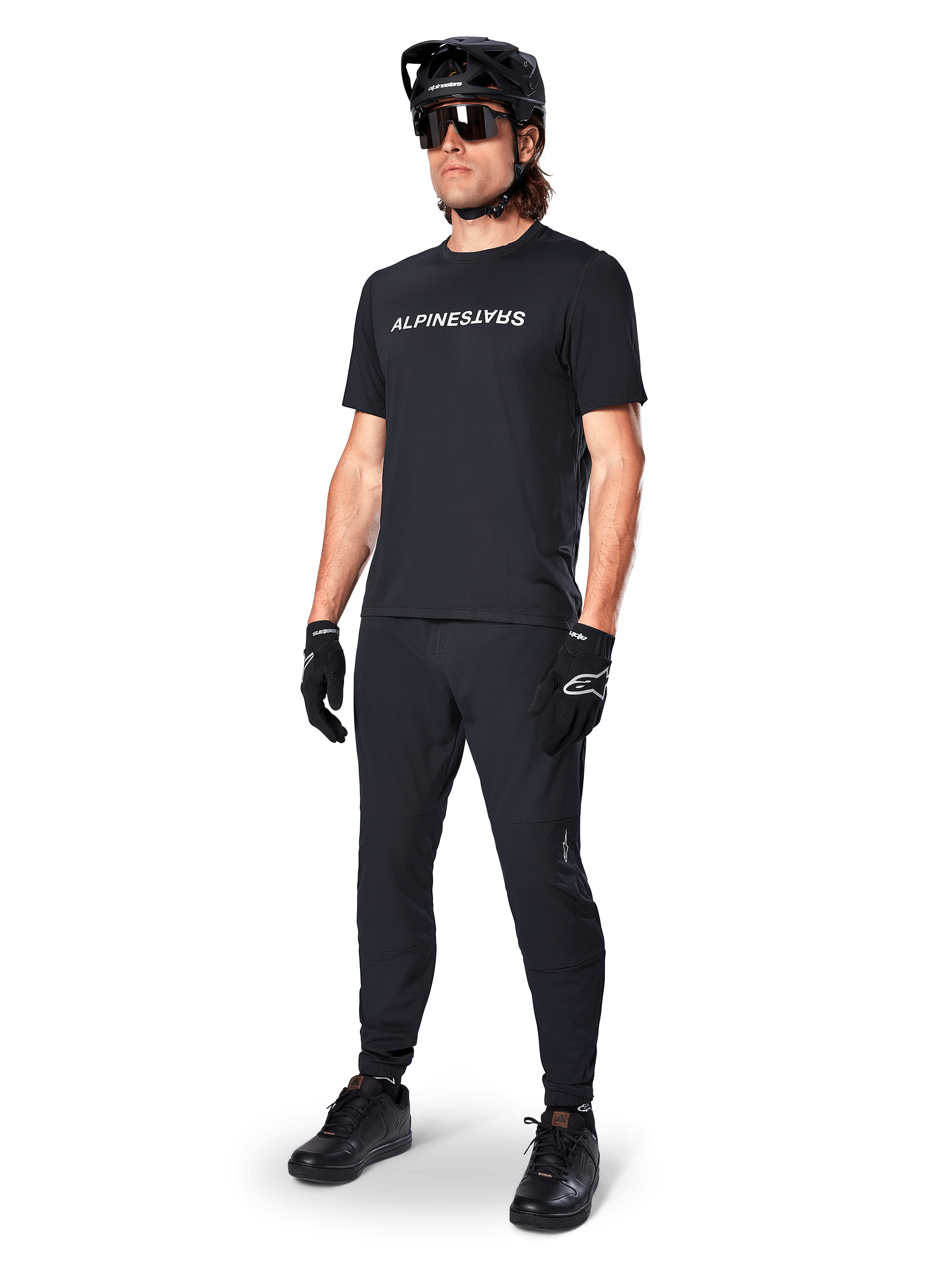Maillot à manches courtes Alpinestars A-Dura Switch, noir, porté par un mannequin avec pantalon de VTT noir, casque et gants assortis, arborant le logo Alpinestars blanc sur la poitrine, vêtement de performance pour le VTT