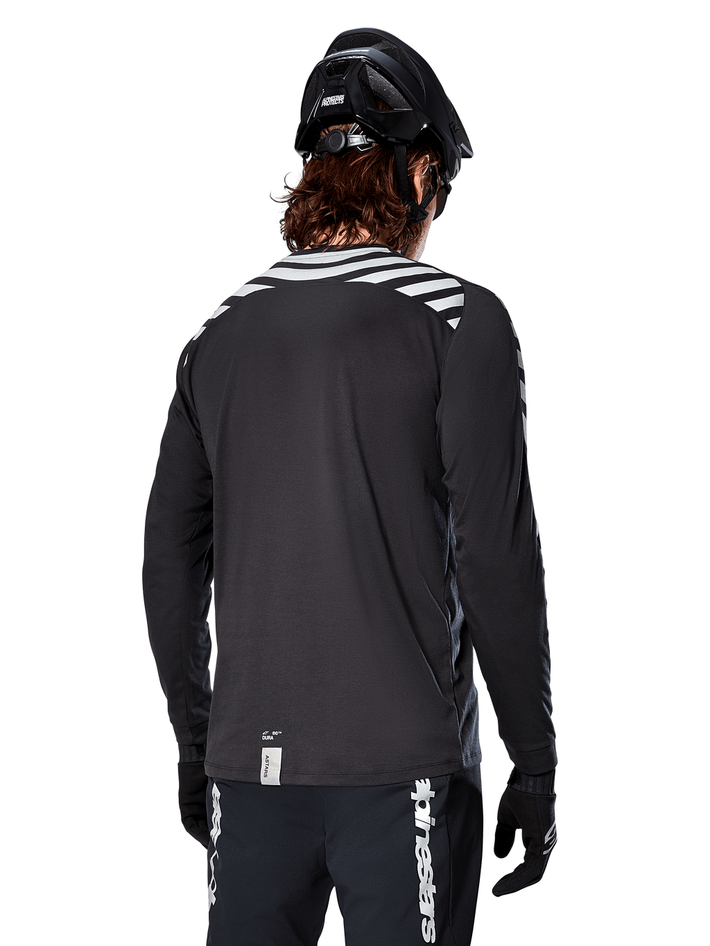 Maillot à manches longues Alpinestars A-Dura Dri Oscar, Noir réfléchissant, vue arrière montrant des rayures diagonales réfléchissantes sur les épaules et un pan arrière plus long, porté avec un casque et des gants de VTT noirs, équipement technique pour le VTT