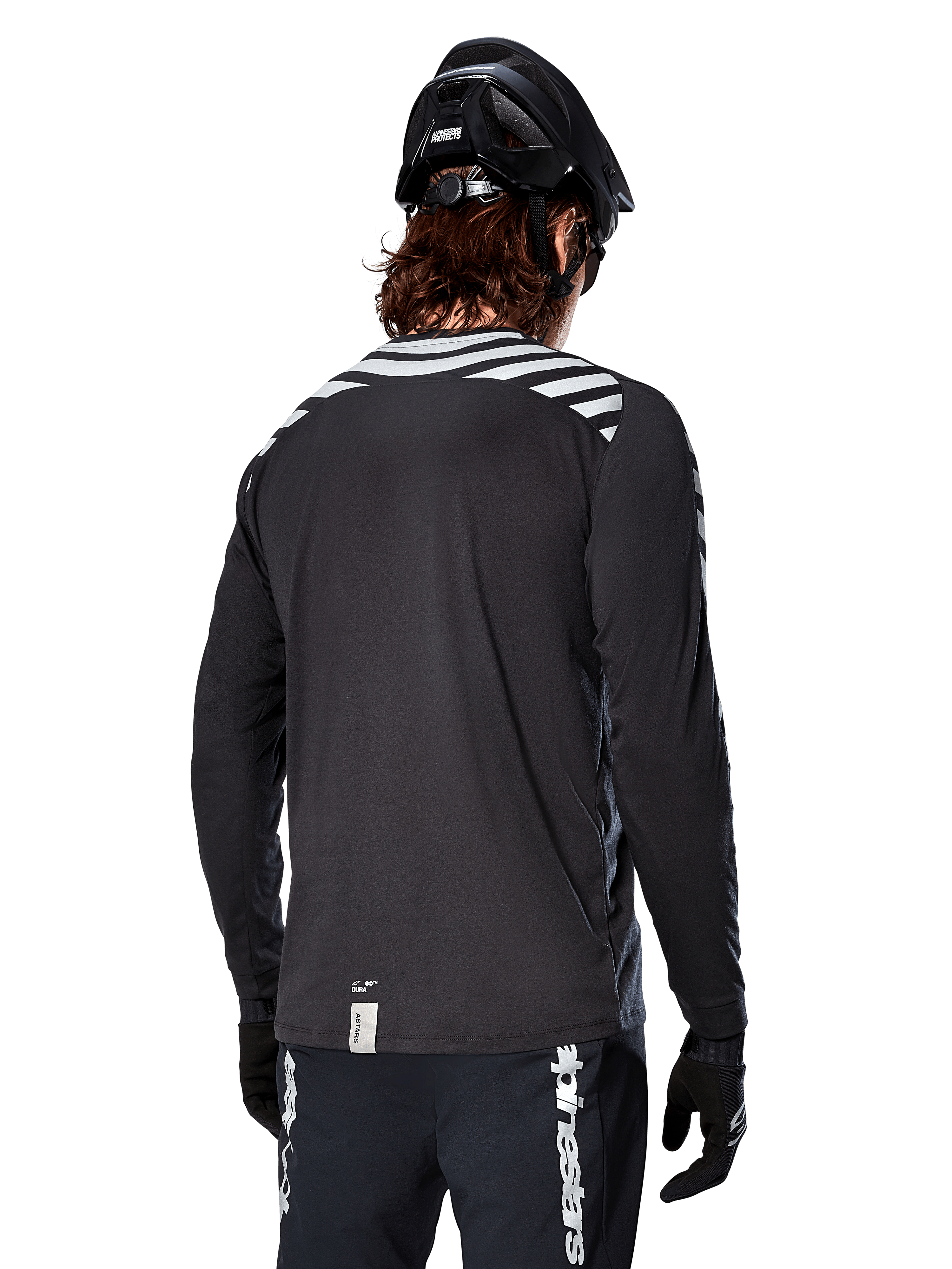 Maillot à manches longues Alpinestars A-Dura Dri Oscar, Noir réfléchissant, vue arrière montrant des rayures diagonales réfléchissantes sur les épaules et un pan arrière plus long, porté avec un casque et des gants de VTT noirs, équipement technique pour le VTT