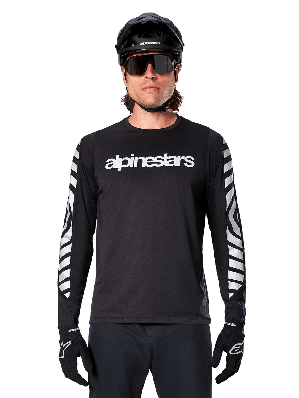 Cycliste portant le maillot à manches longues Alpinestars A-Dura Dri Oscar, Noir Réfléchissant, avec lettrage Alpinestars blanc sur la poitrine et graphismes argentés réfléchissants sur les manches, accompagné d'un casque de VTT noir, de lunettes de soleil et de gants noirs, tenue de cyclisme haute performance
