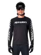 Cycliste portant le maillot à manches longues Alpinestars A-Dura Dri Oscar, Noir Réfléchissant, avec lettrage Alpinestars blanc sur la poitrine et graphismes argentés réfléchissants sur les manches, accompagné d'un casque de VTT noir, de lunettes de soleil et de gants noirs, tenue de cyclisme haute performance