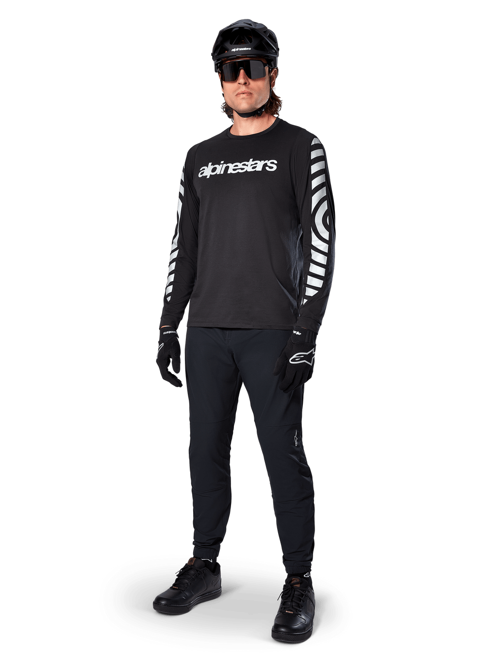 Maillot à manches longues Alpinestars A-Dura Dri Oscar, noir réfléchissant, arborant un lettrage Alpinestars blanc sur la poitrine et des motifs graphiques réfléchissants sur les manches, porté avec un pantalon de VTT noir, un casque et des gants, équipement technique de VTT