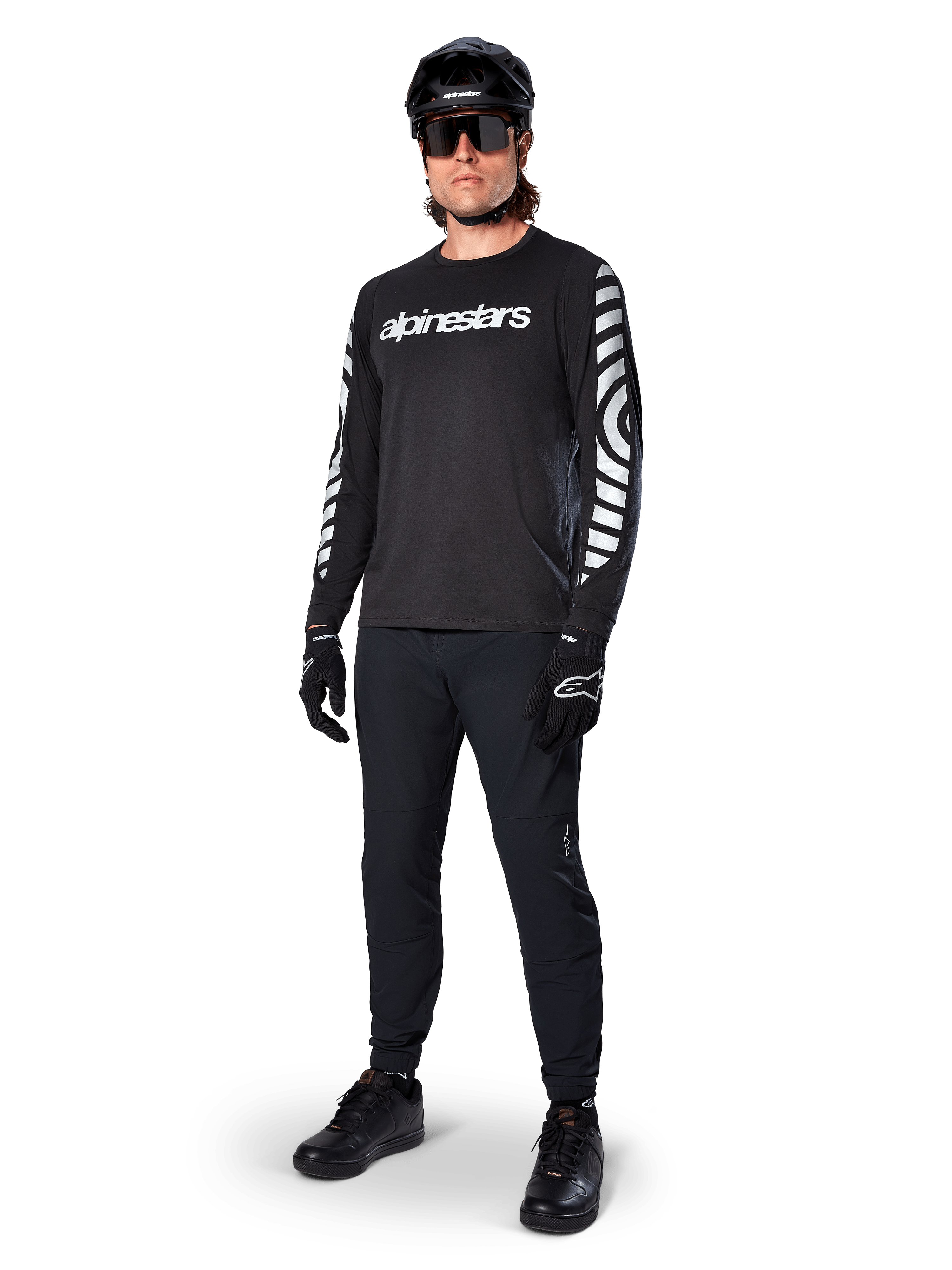 Maillot à manches longues Alpinestars A-Dura Dri Oscar, noir réfléchissant, arborant un lettrage Alpinestars blanc sur la poitrine et des motifs graphiques réfléchissants sur les manches, porté avec un pantalon de VTT noir, un casque et des gants, équipement technique de VTT