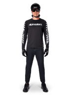 Maillot à manches longues Alpinestars A-Dura Dri Oscar en noir réfléchissant, porté avec un casque noir et des lunettes de soleil, avec logo blanc sur la poitrine et motifs graphiques réfléchissants sur les manches, équipement de VTT pour le tout-terrain