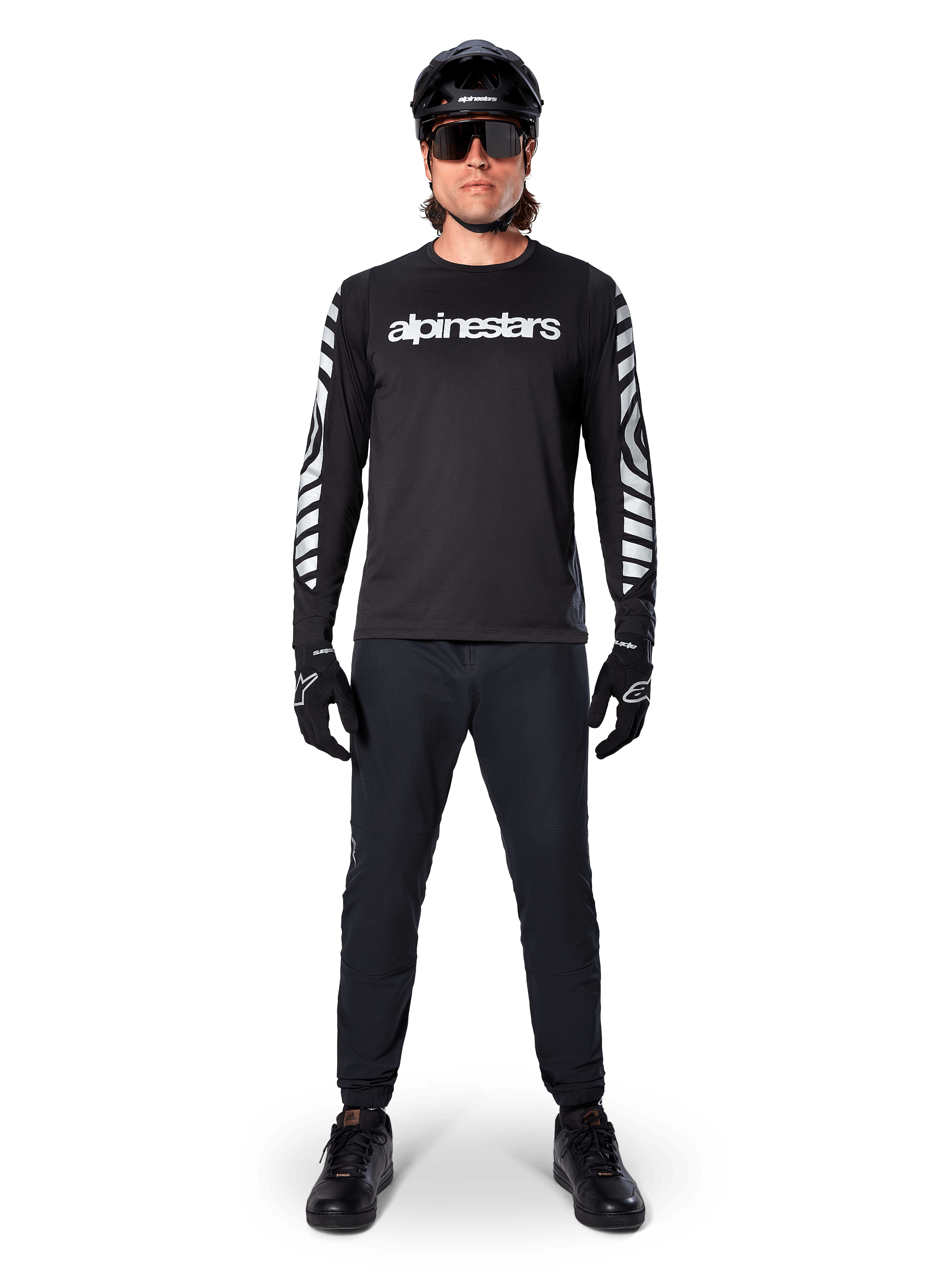 Maillot à manches longues Alpinestars A-Dura Dri Oscar en noir réfléchissant, porté avec un casque noir et des lunettes de soleil, avec logo blanc sur la poitrine et motifs graphiques réfléchissants sur les manches, équipement de VTT pour le tout-terrain