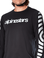 Maillot à manches longues Alpinestars A-Dura Dri Oscar, noir réfléchissant, vue rapprochée montrant le logo Alpinestars blanc sur la poitrine et les graphiques circulaires réfléchissants sur les manches, vêtement technique de cyclisme pour le VTT