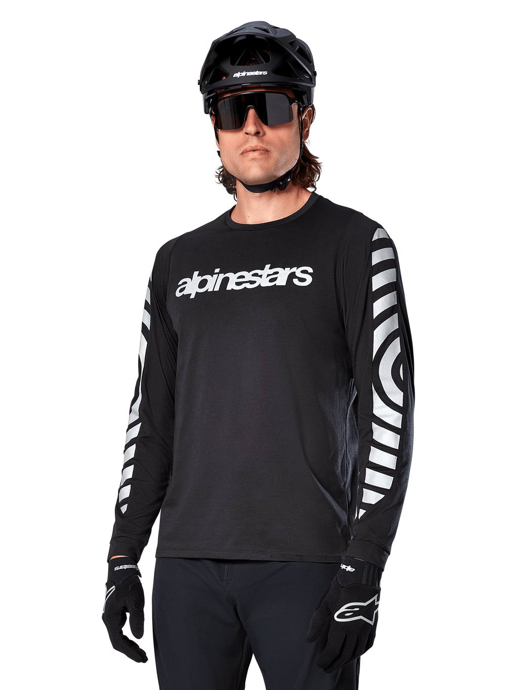 Maillot à manches longues Alpinestars A-Dura Dri Oscar, maillot de cyclisme VTT, noir réfléchissant, avec logo blanc sur la poitrine et graphismes circulaires réfléchissants sur les manches, porté avec un casque noir et des lunettes de soleil, vêtement technique évacuant l'humidité pour le VTT tout-terrain