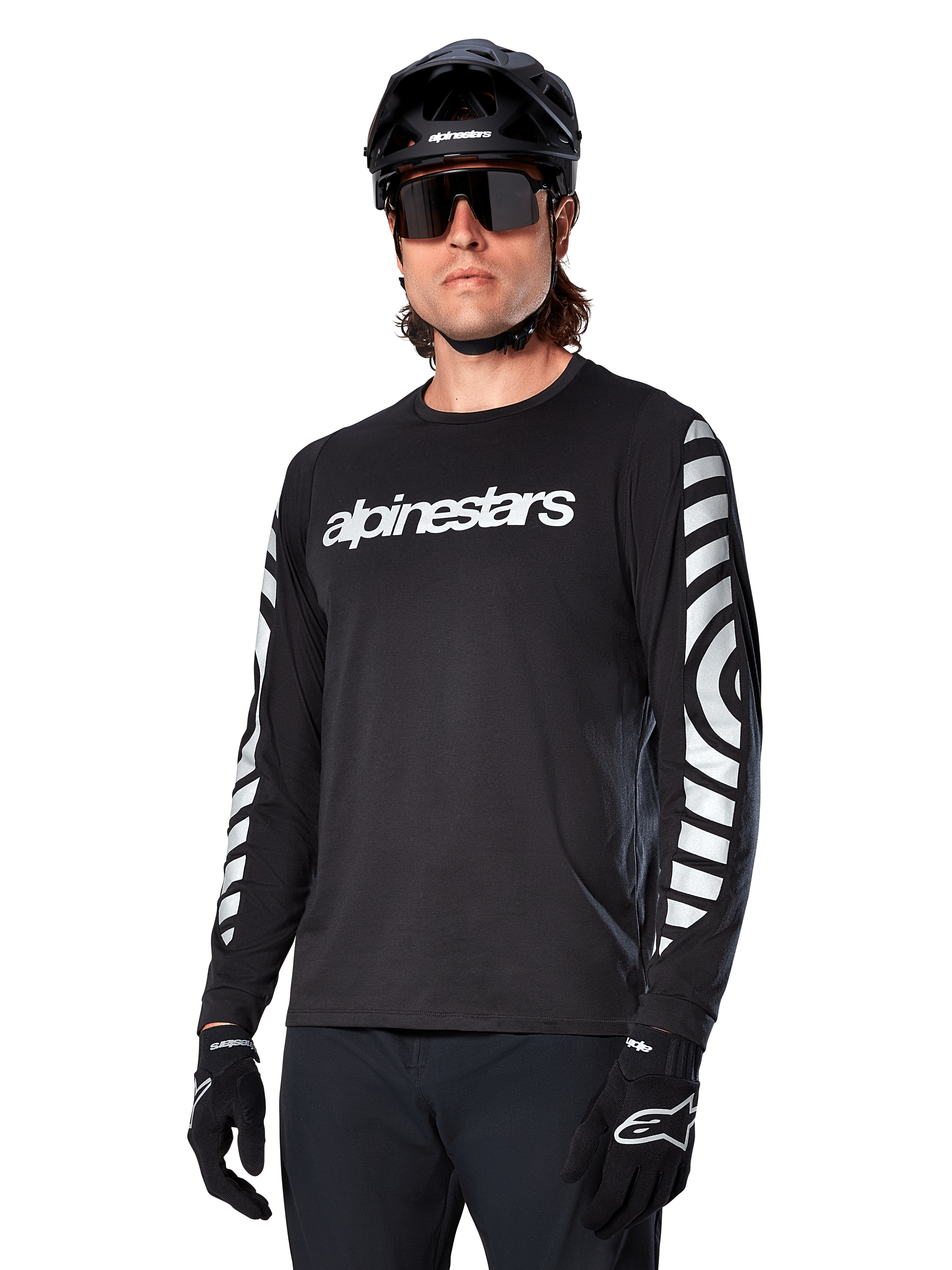 Maillot à manches longues Alpinestars A-Dura Dri Oscar, maillot de cyclisme VTT, noir réfléchissant, avec logo blanc sur la poitrine et graphismes circulaires réfléchissants sur les manches, porté avec un casque noir et des lunettes de soleil, vêtement technique évacuant l'humidité pour le VTT tout-terrain